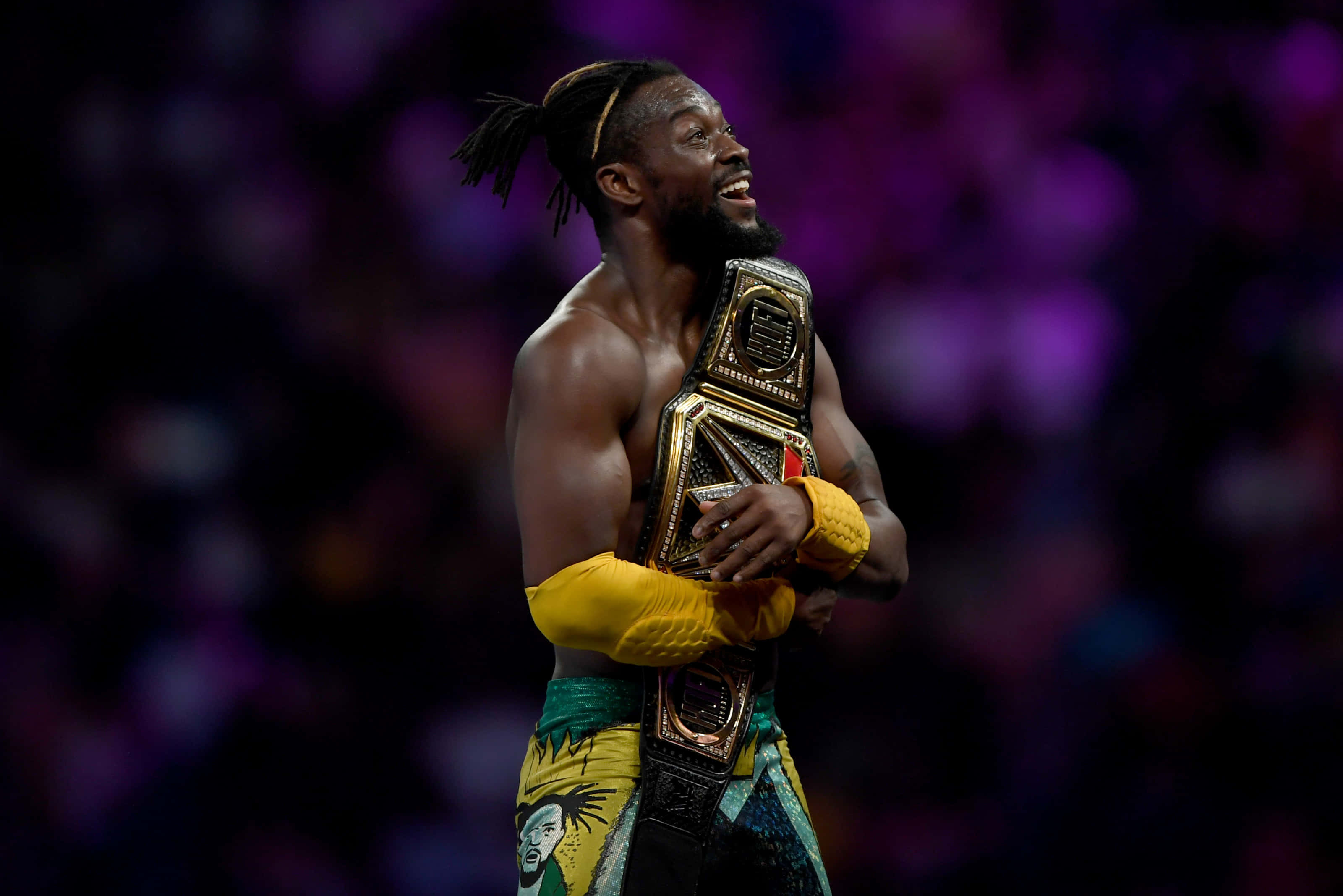 WWE 桌布 壁紙 — 一位勝利的摔角手在充滿活力的紫色模糊競技場背景下，手持冠軍腰帶，滿臉喜悅。
