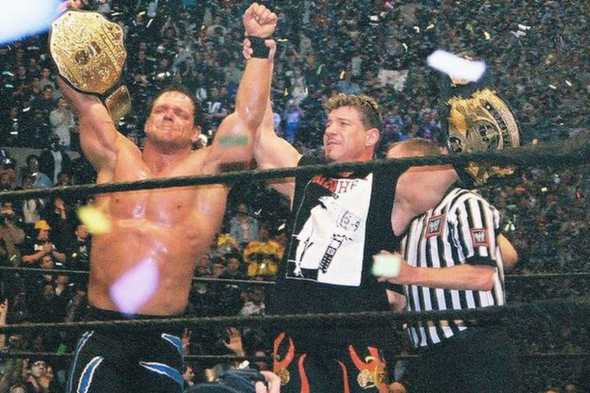 WWE 桌布 壁紙 — 一位勝利的摔角手在擂台上高舉冠軍腰帶，彩紙飄落，裁判舉起他的手臂以示勝利。
