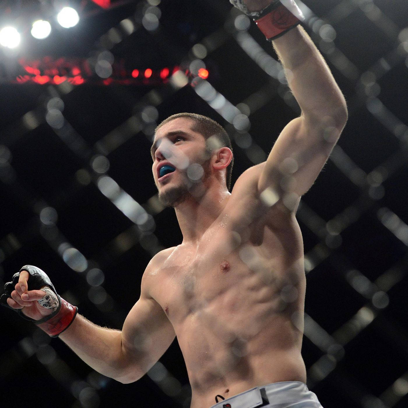 UFC 桌布 壁紙 — 一位勝利的混合武術家在一盞明亮的八角籠中高舉手臂慶祝勝利。