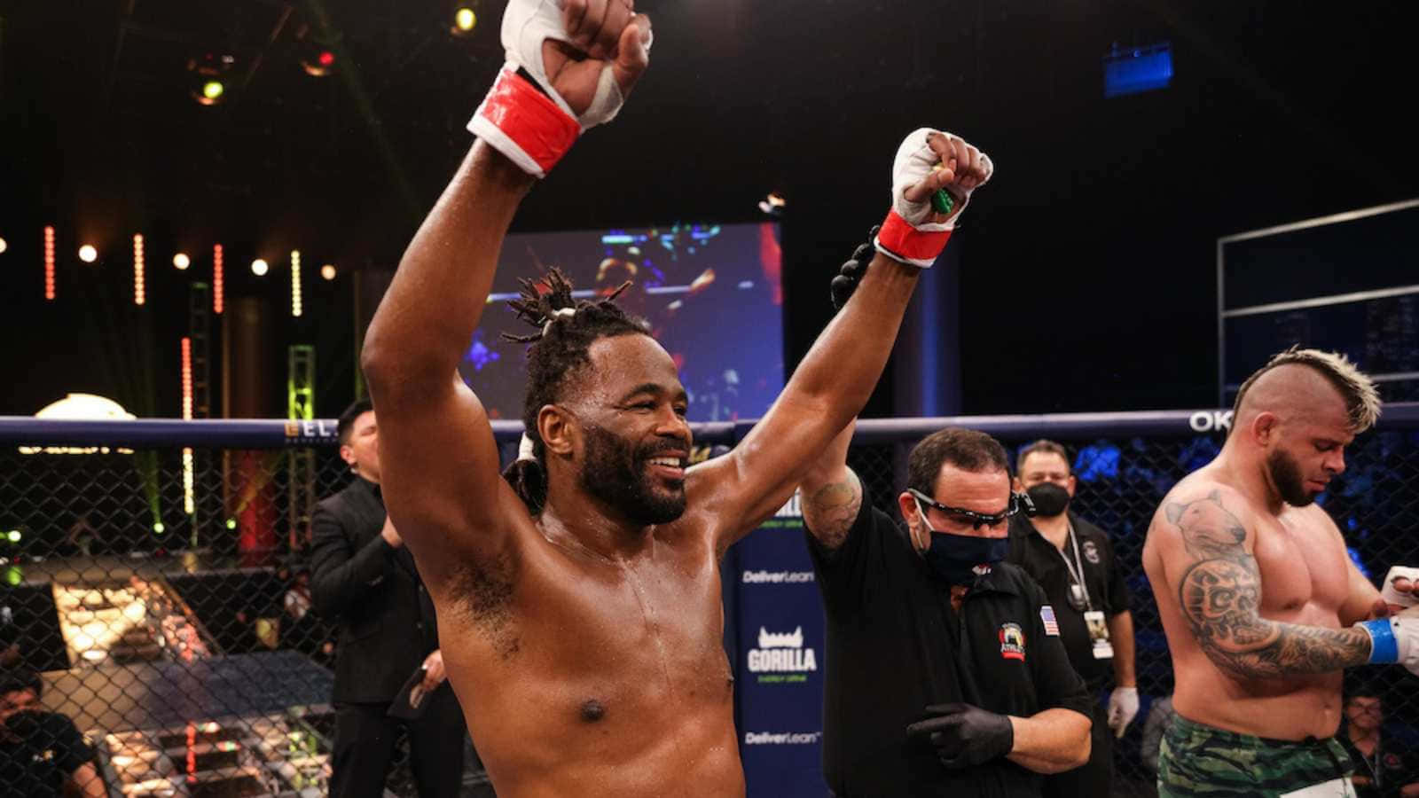 Champion 桌布 壁紙 — 一位勝利的混合武術家在明亮照明的八角籠內舉起拳頭慶祝勝利，附近有裁判和對手。