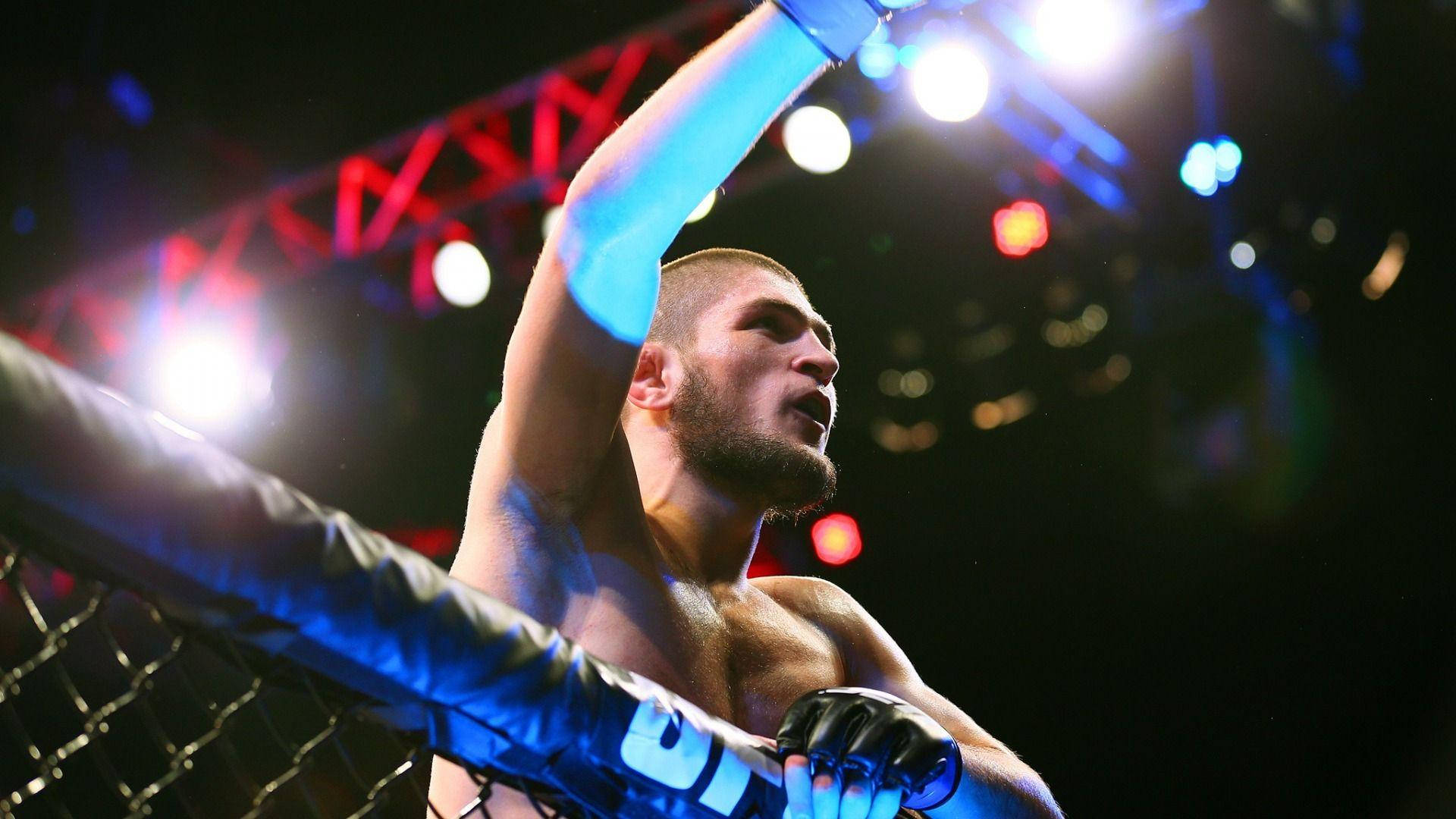 UFC 桌布 壁紙 — 一位勝利的混合武術家在明亮的八角籠內高舉手臂慶祝勝利。