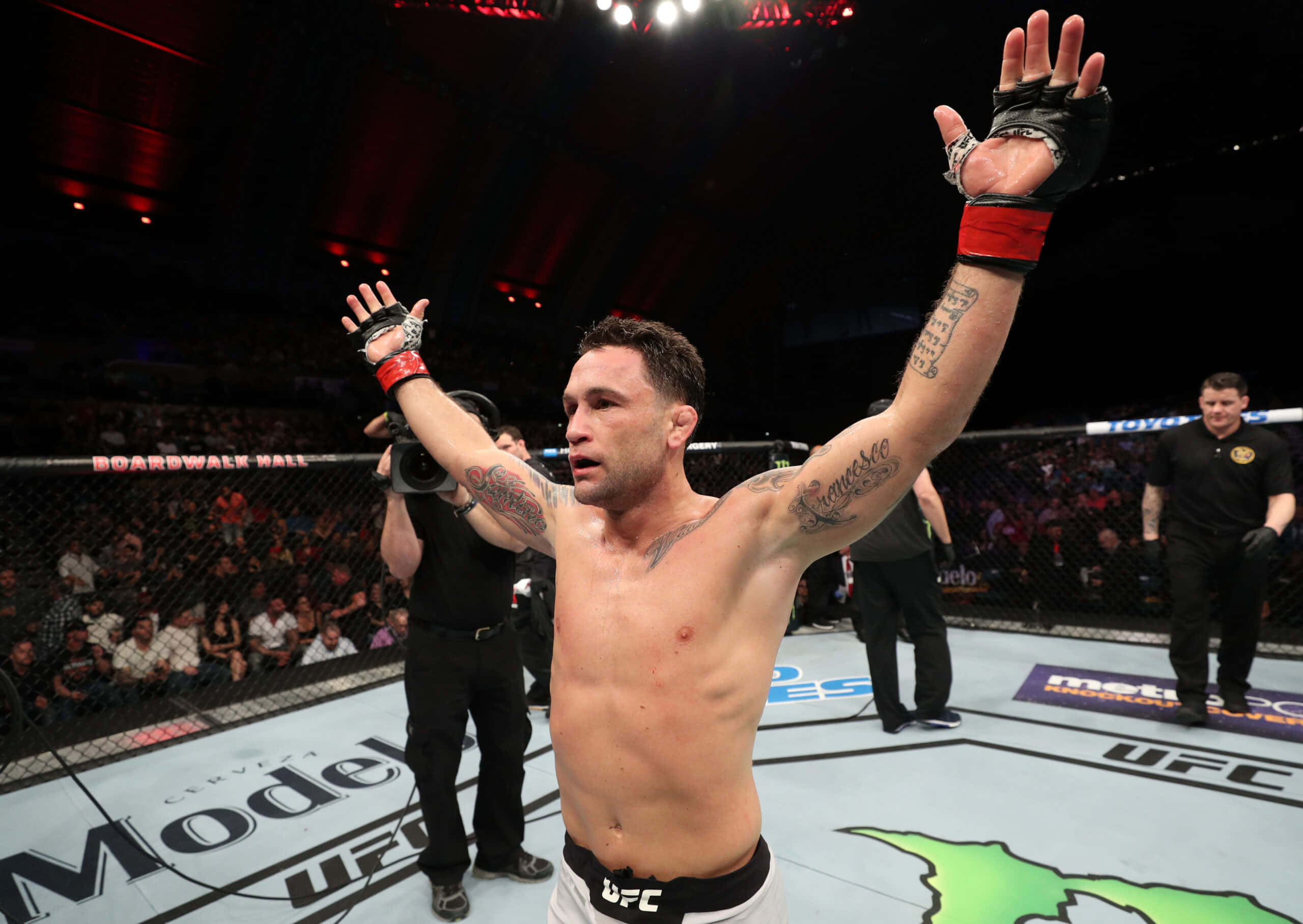 UFC 桌布 壁紙 — 一位勝利的混合武術家在明亮的競技場燈光下，在UFC八角籠內高舉雙臂慶祝勝利。
