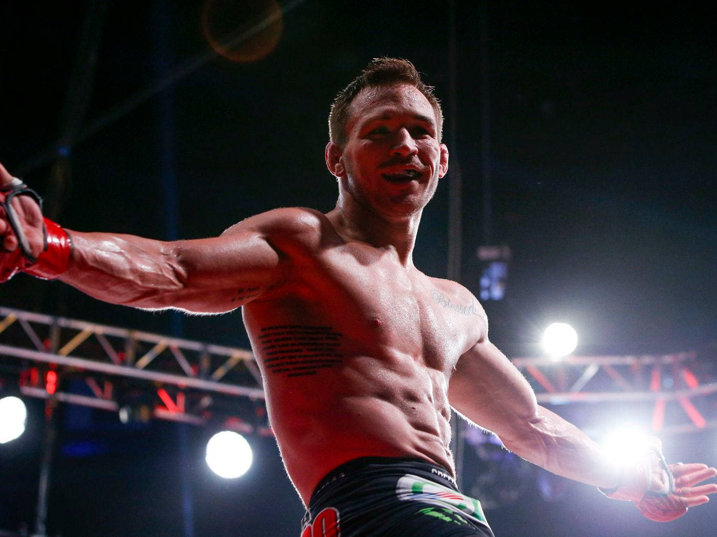 Michael Chandler 桌布 壁紙 — 一位勝利的混合武術家在明亮的競技場燈光下，在擂台上張開雙臂慶祝勝利。