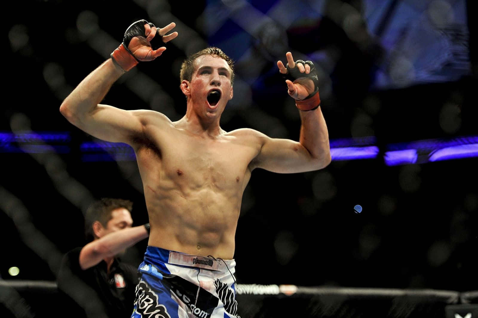 UFC 桌布 壁紙 — 一位勝利的混合武術家在昏暗的八角籠內高舉雙臂勝利呼喊。