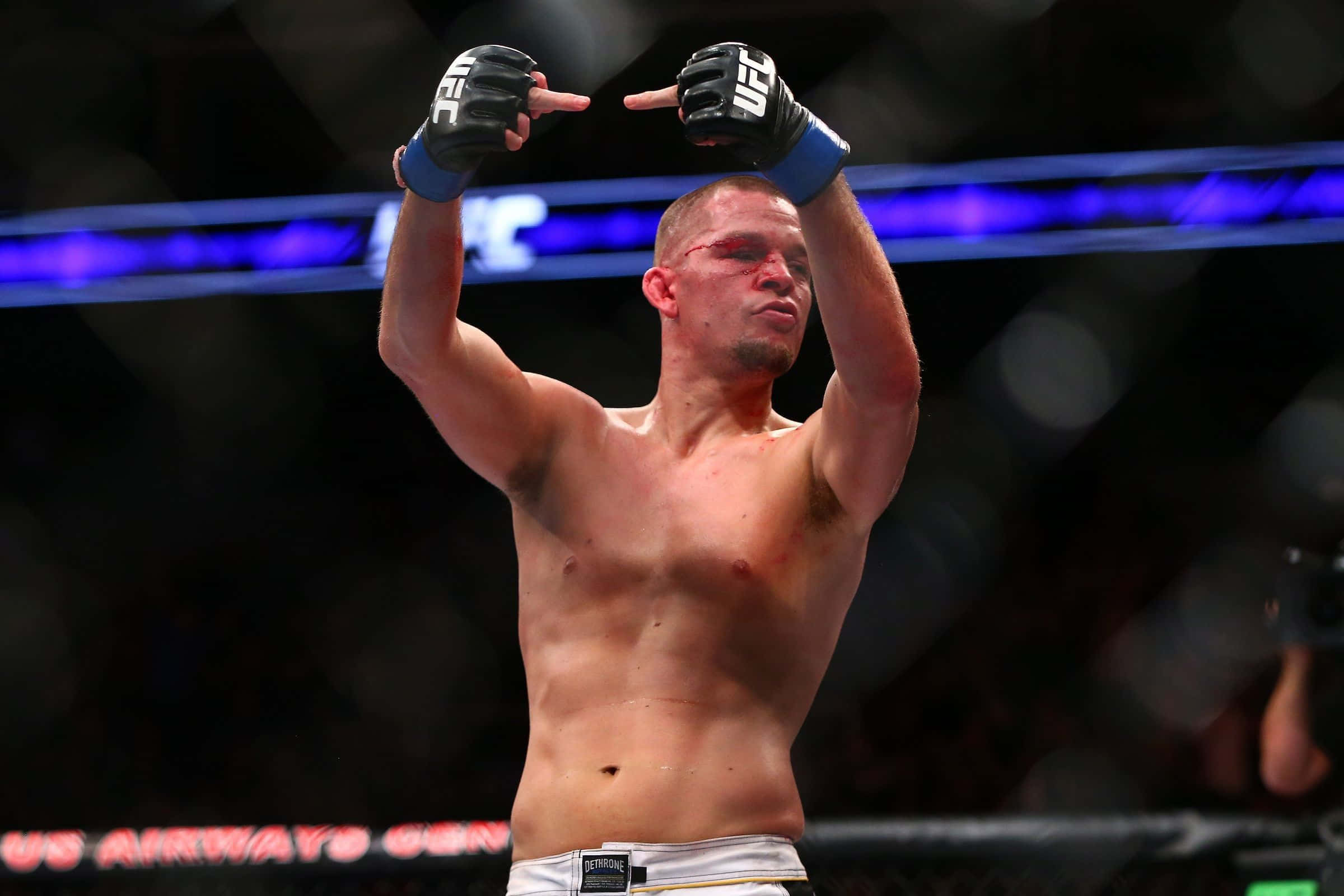 UFC 桌布 壁紙 — 一位勝利的混合武術家在燈光明亮的八角籠內，舉起戴著手套的雙手慶祝勝利，背景是模糊的人群和藍色燈光。