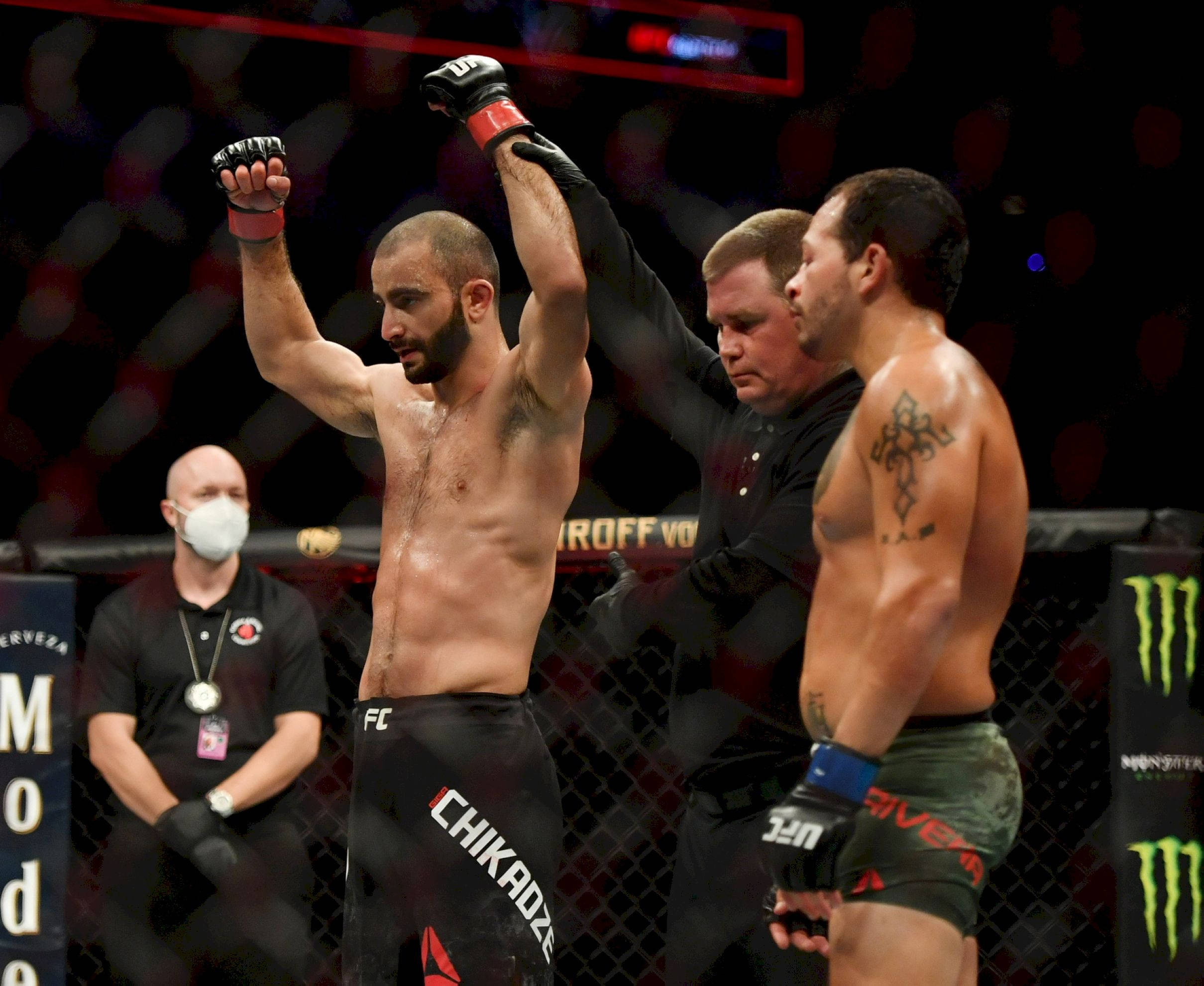 UFC 桌布 壁紙 — 一位勝利的混合武術家高舉雙臂慶祝勝利，裁判在燈光明亮的八角籠內舉起他的手。