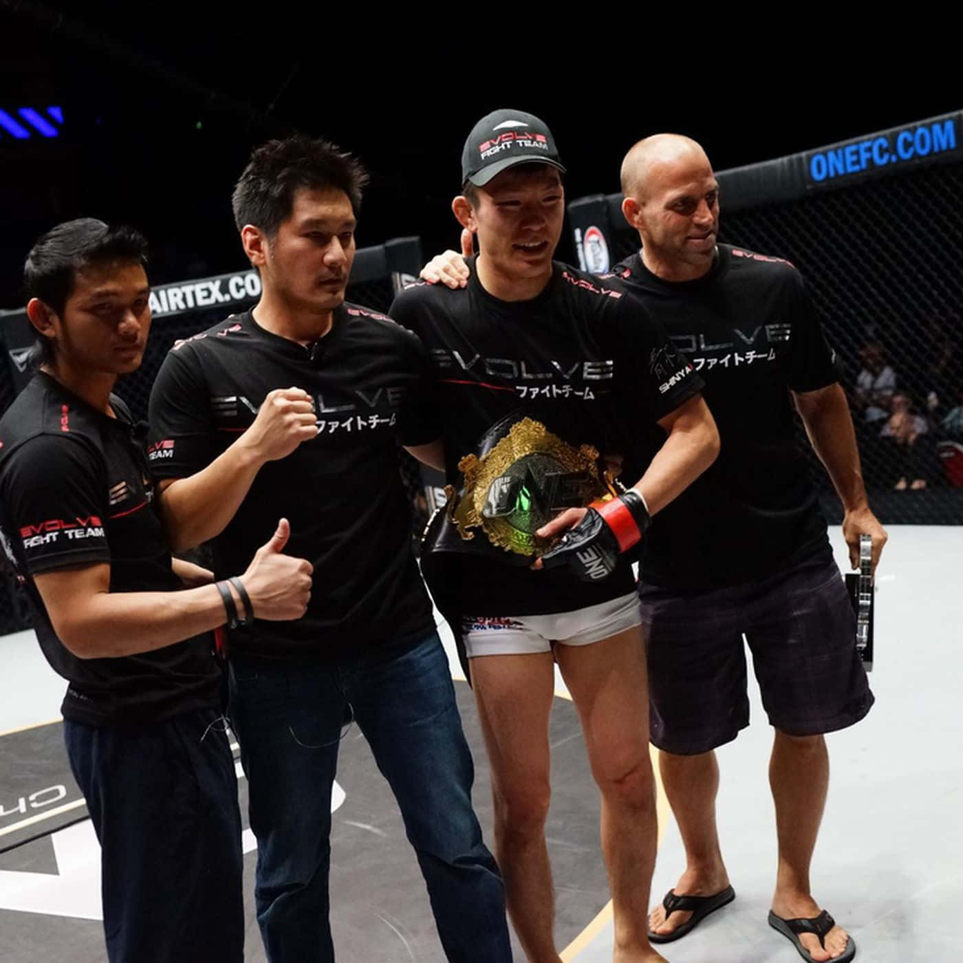 MMA 桌布 壁紙 — 一位勝利的混合武術選手在MMA八角籠內被團隊包圍，手持冠軍腰帶。