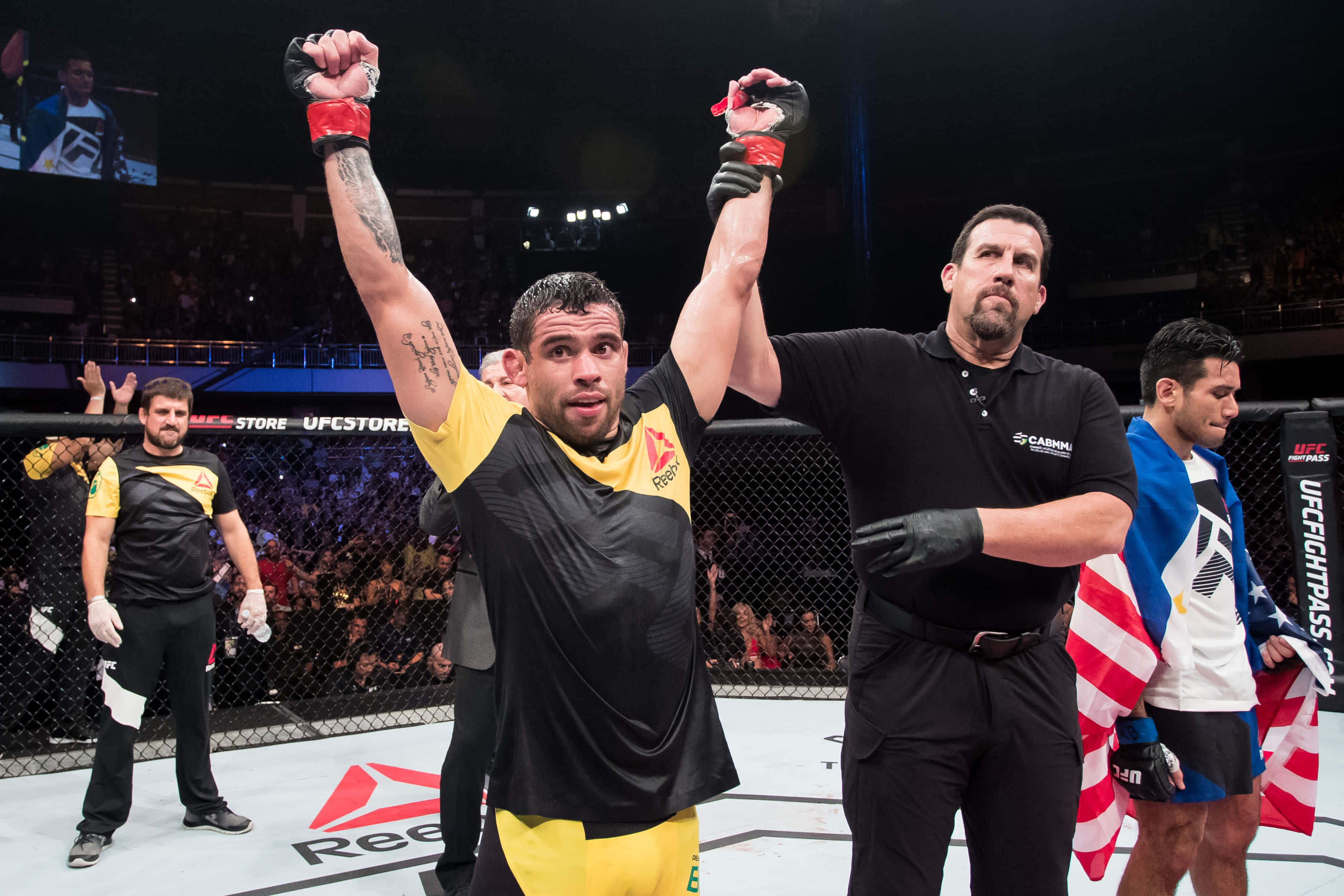 UFC 桌布 壁紙 — 一位勝利的混合武術選手在UFC八角籠中高舉雙臂慶祝勝利，裁判也舉起他的手。