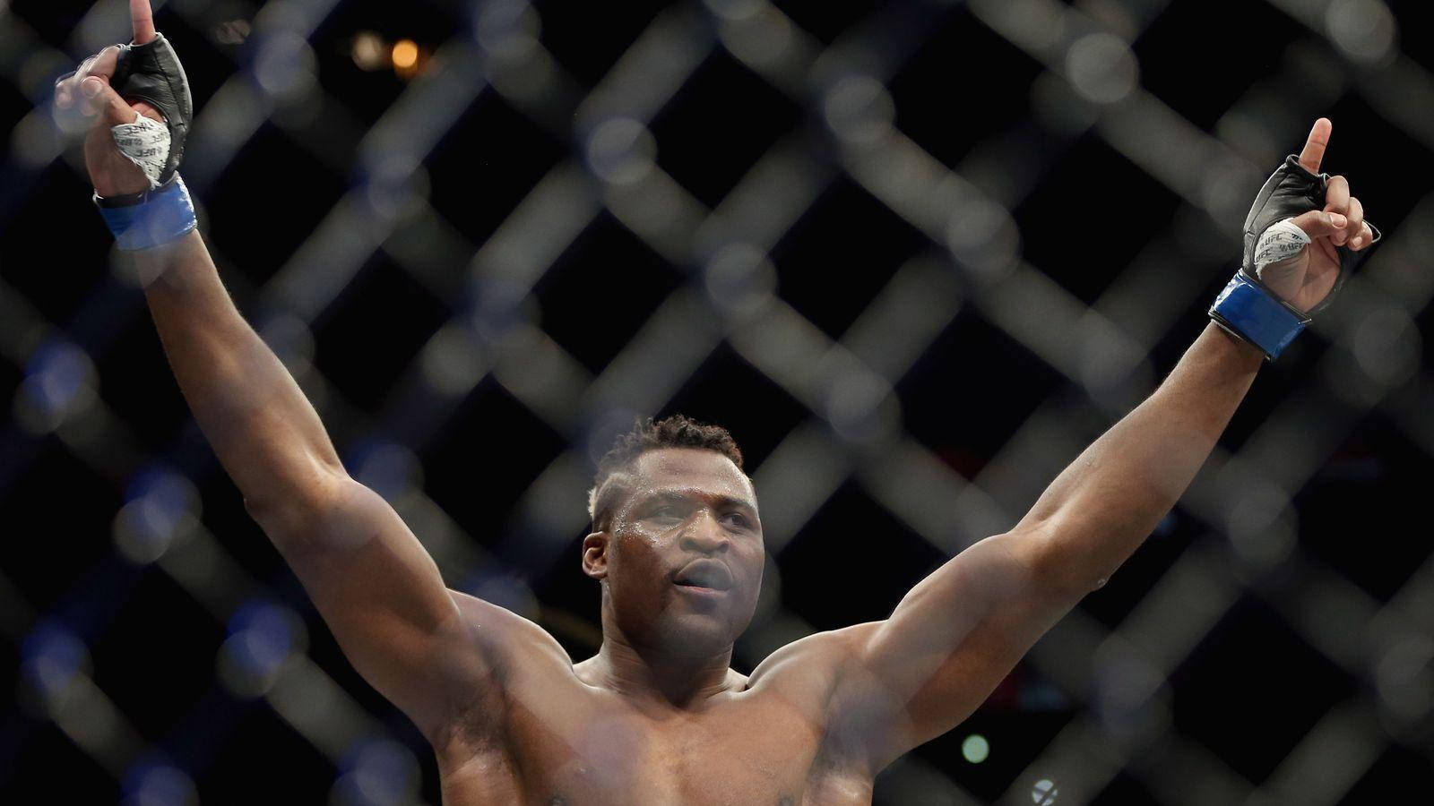 MMA 桌布 壁紙 — 一位勝利的混合武術選手在昏暗的八角籠內高舉雙臂慶祝勝利。