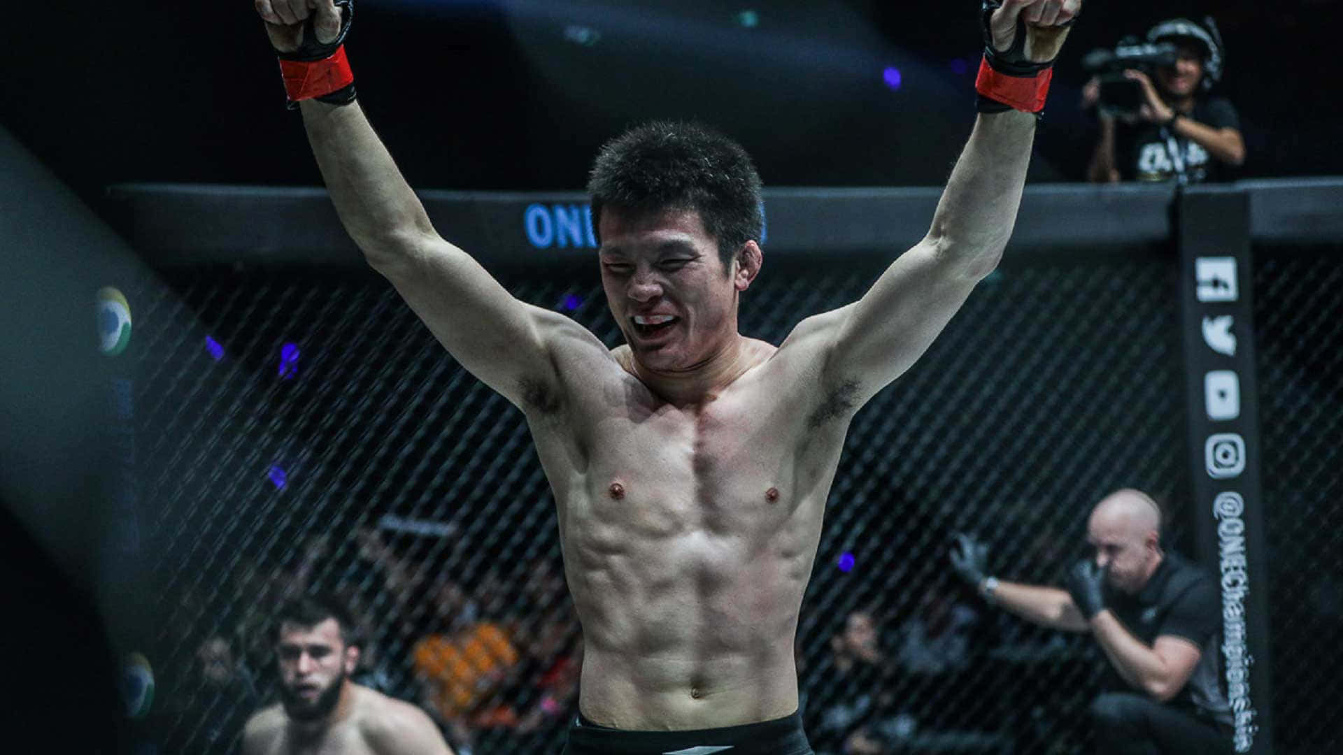 martial arts 桌布 壁紙 — 一位勝利的混合武術選手在昏暗的八角籠內，舉起雙臂慶祝勝利，周圍有藍色發光燈光。