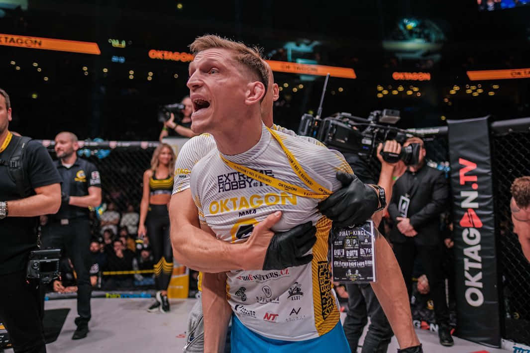 UFC 桌布 壁紙 — 一位勝利的混合武術選手在經過一場艱苦的比賽後，被隊友抬出八角籠，並發出勝利的吶喊。