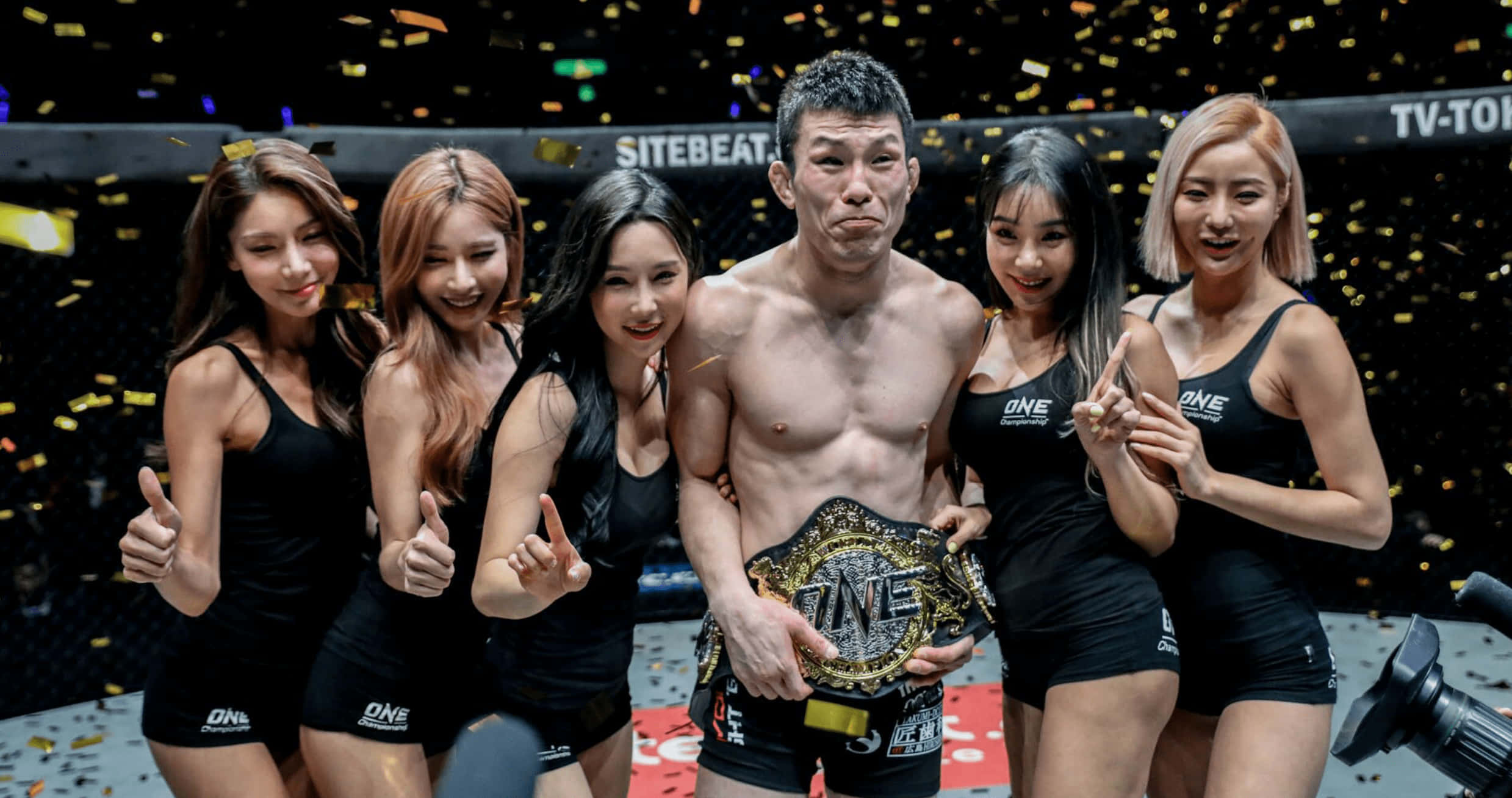 martial arts 桌布 壁紙 — 一位勝利的男性拳手在MMA擂台上高舉冠軍腰帶，被五位身穿黑色服裝的微笑女性圍繞，金色紙屑飄落。