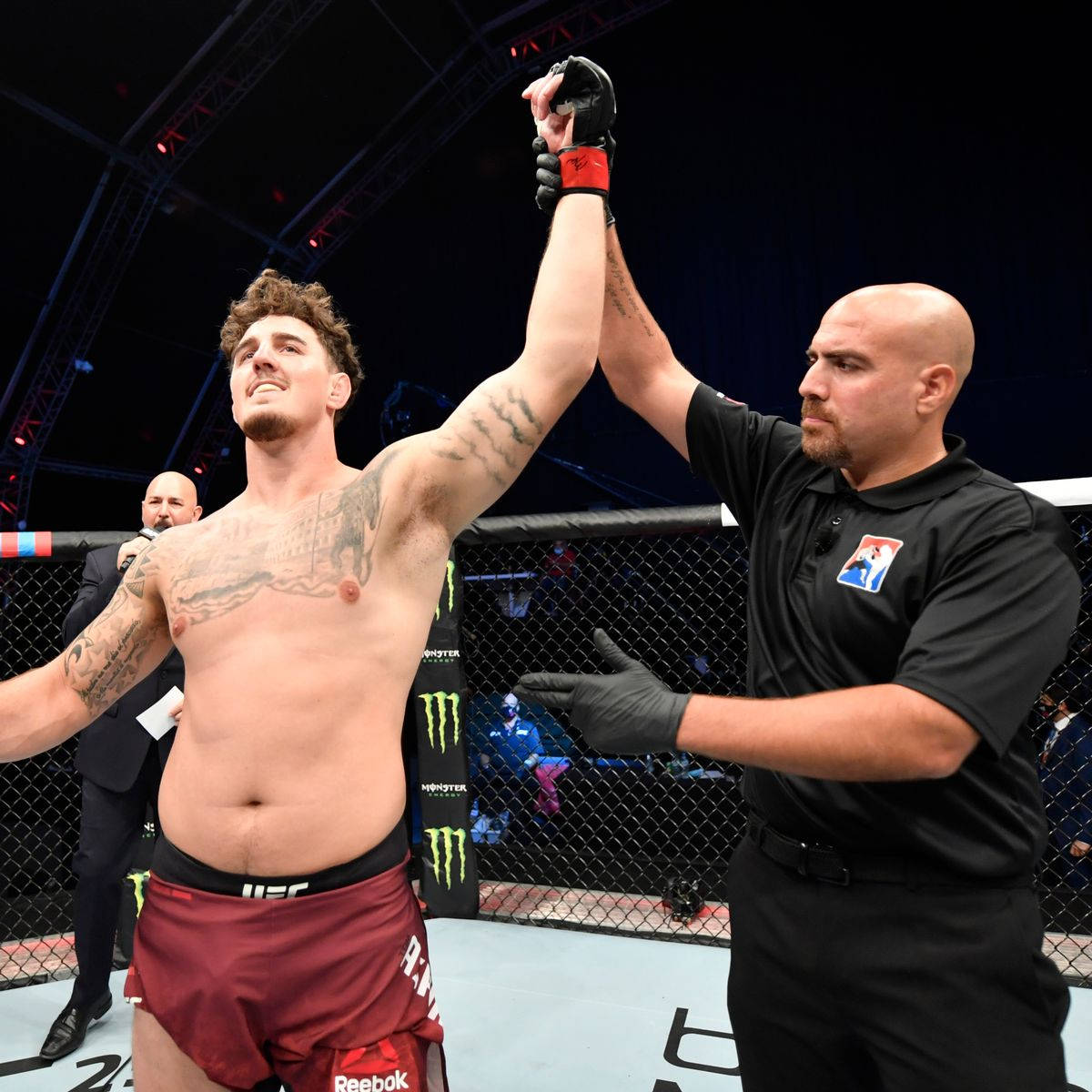 UFC 桌布 壁紙 — 一位勝利的綜合格鬥家在明亮的競技場燈光下，裁判在八角籠中舉起他的手臂慶祝。
