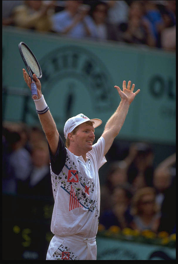 Tennis 桌布 壁紙 — 一位勝利的網球選手在紅土球場上高舉球拍和手慶祝勝利，背景是模糊的歡呼觀眾。