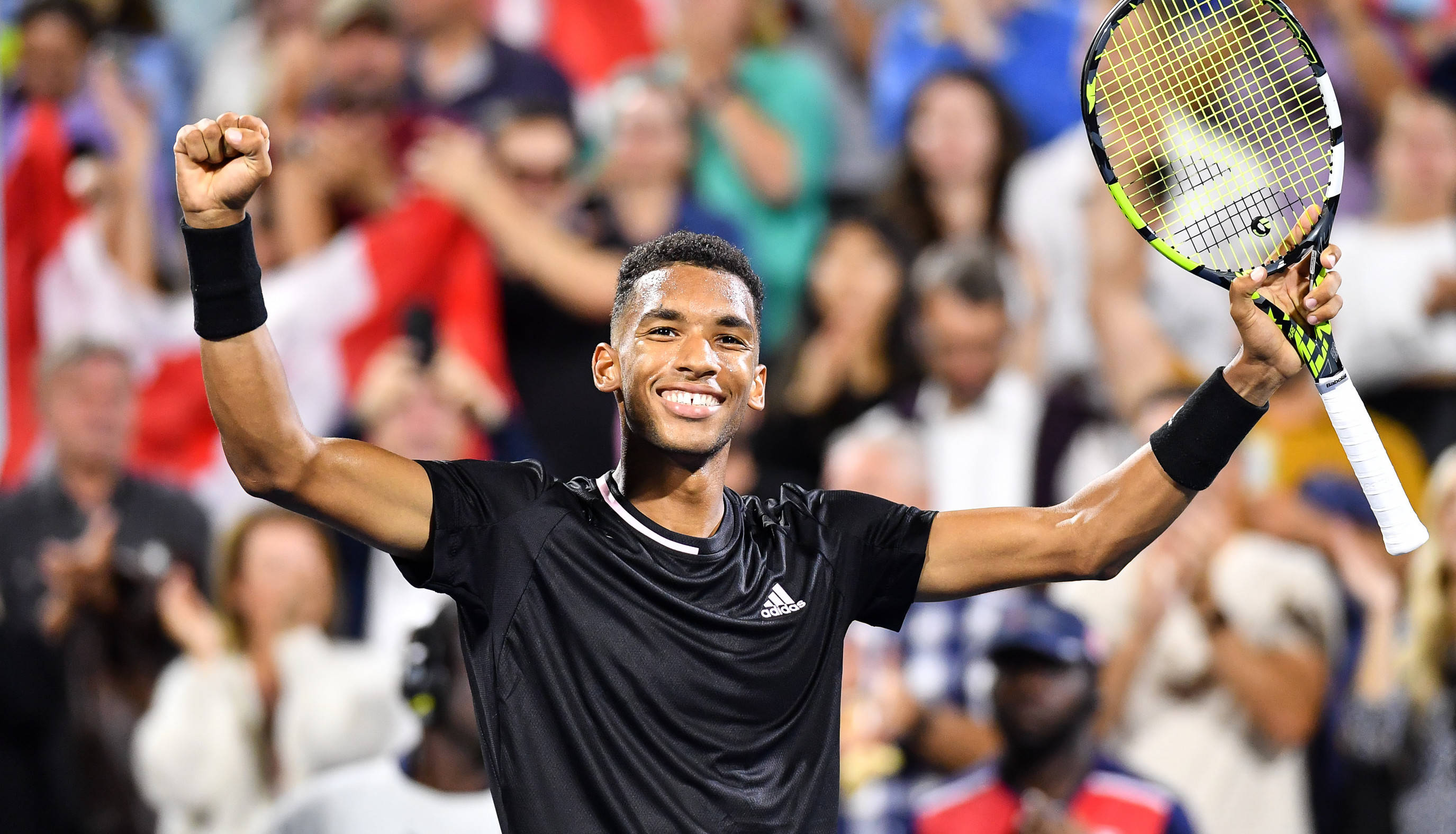 felix auger aliassime 桌布 壁紙 — 一位勝利的網球選手在體育場燈光下高舉拳頭和球拍慶祝勝利。