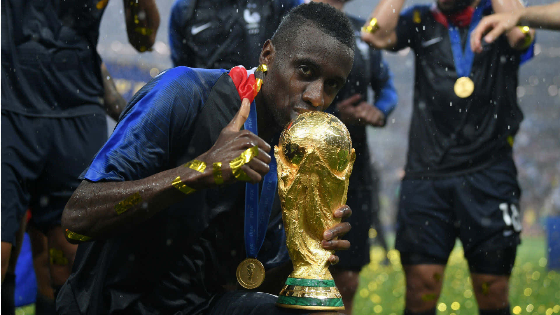 Football Players 桌布 壁紙 — 一位勝利的足球員在金色紙屑灑落球場之際，親吻閃閃發光的世界盃獎盃。