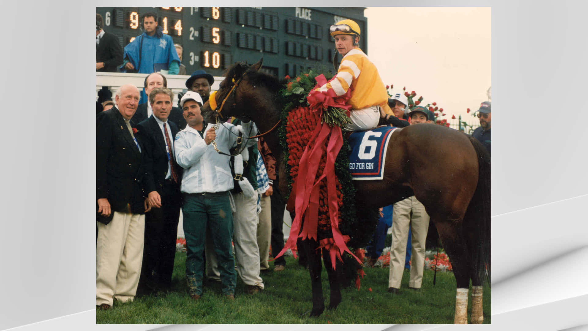 Kentucky Derby 桌布 壁紙 — 一位勝利的騎師身穿黃色綢緞，騎著一匹裝飾著紅玫瑰和6號鞍布的棕色賽馬，工作人員和官員在草地上慶祝。