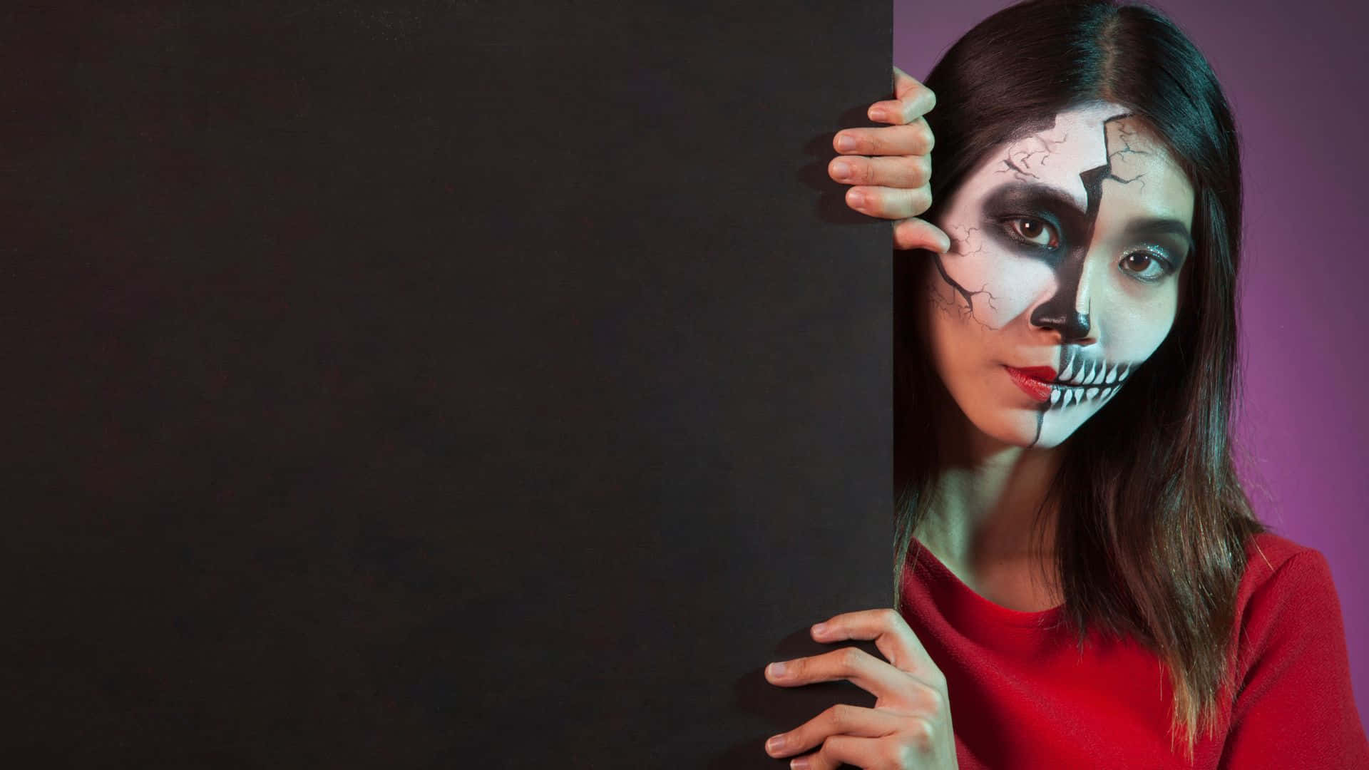 Horror Costumes 桌布 壁紙 — 一位化了一半骷髏妝容的女性從紫色背景的黑色面板後探出頭來。