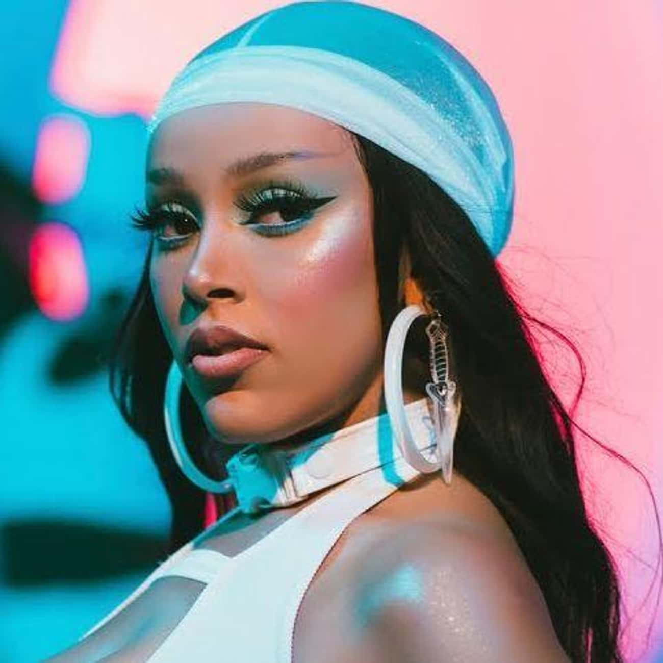 Doja Cat 桌布 壁紙 — 一位化著大膽妝容、戴著超大圓環耳環的女性，在充滿活力的粉紅色和藍色霓虹燈背景前擺姿勢。