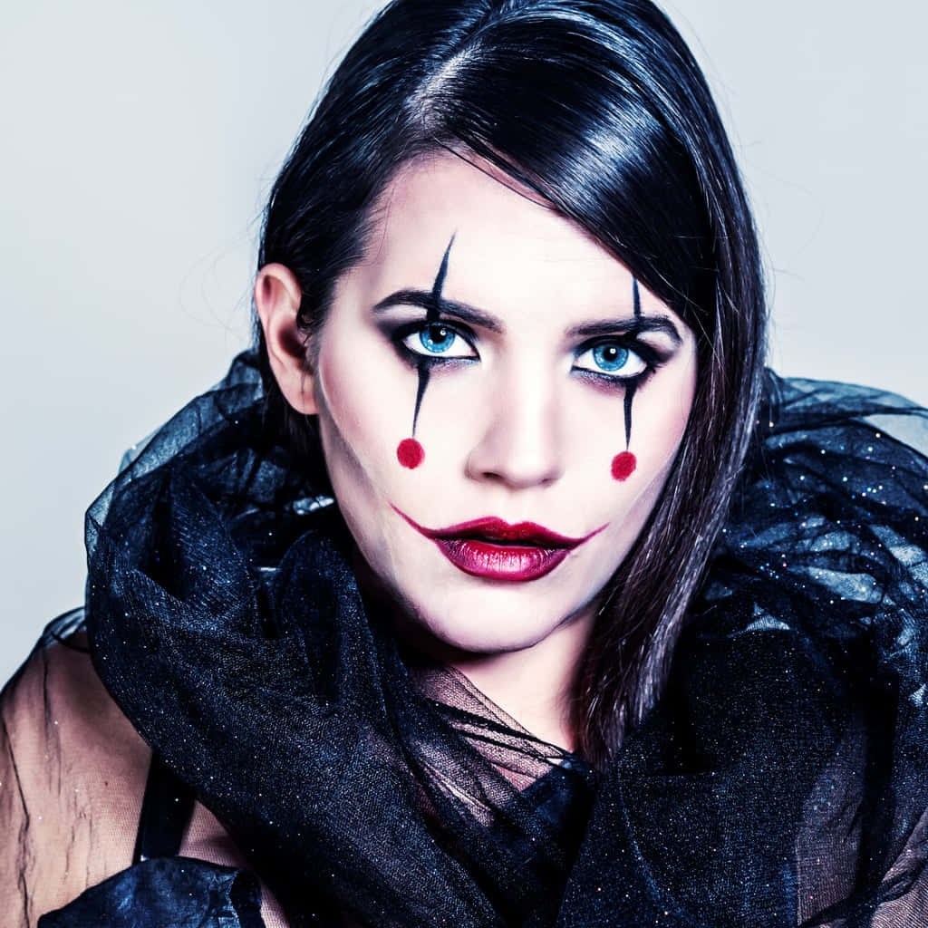 Halloween Face Paint 桌布 壁紙 — 一位化著戲劇性小丑妝容的女性，穿著黑色透視衣物，在素色背景下凝視著鏡頭。
