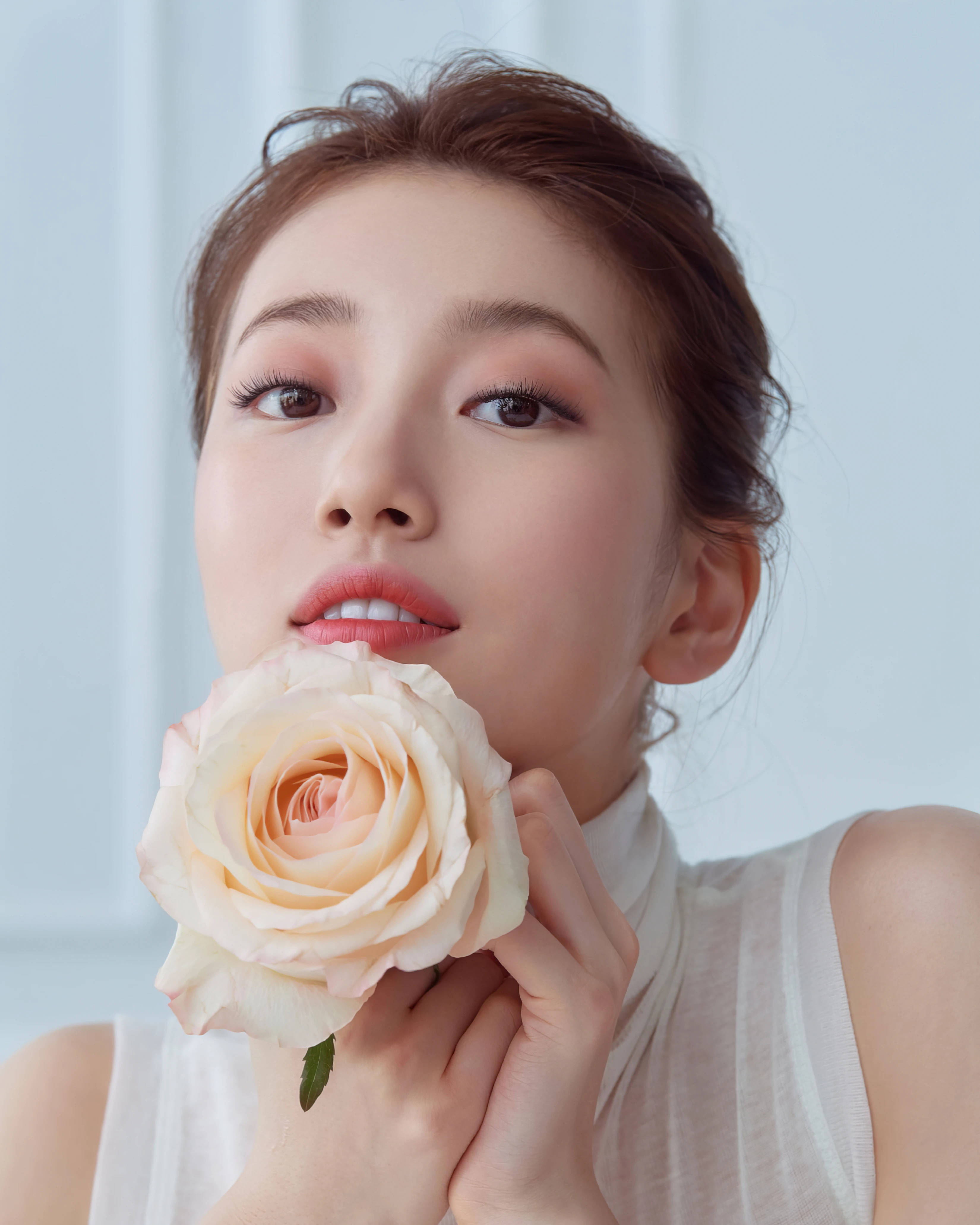 bae 桌布 壁紙 — 一位化著淡妝的女性，在淡藍色背景前，將一朵精緻的蜜桃玫瑰靠近嘴唇。