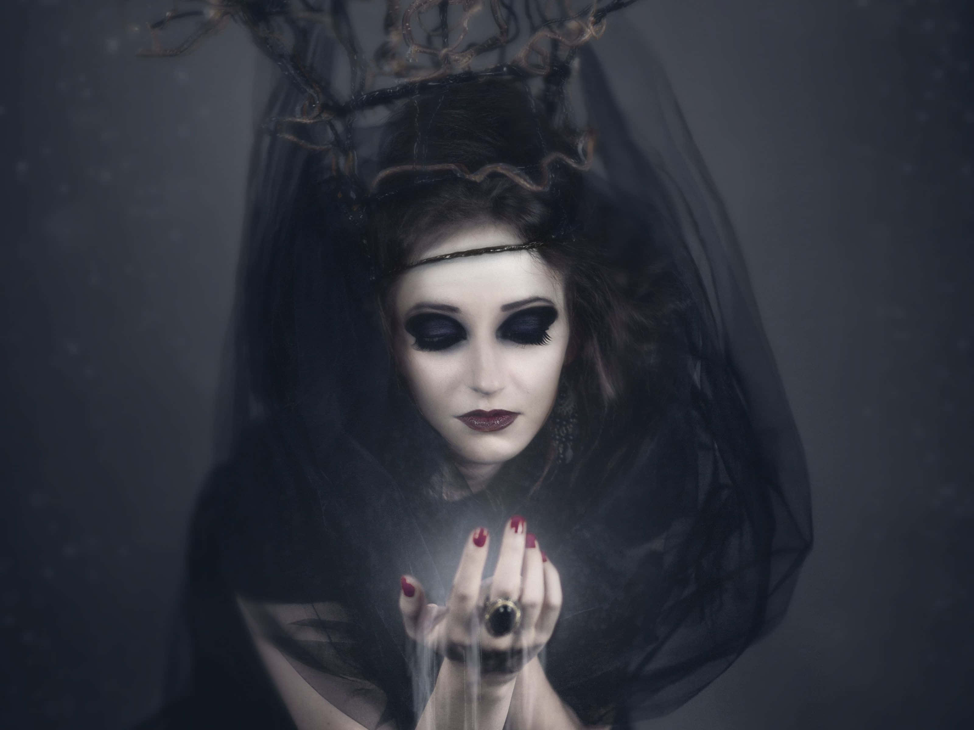 Dark Witch 桌布 壁紙 — 一位化著深色妝容、戴著面紗的女性，在渾濁的水中手持發光球體。