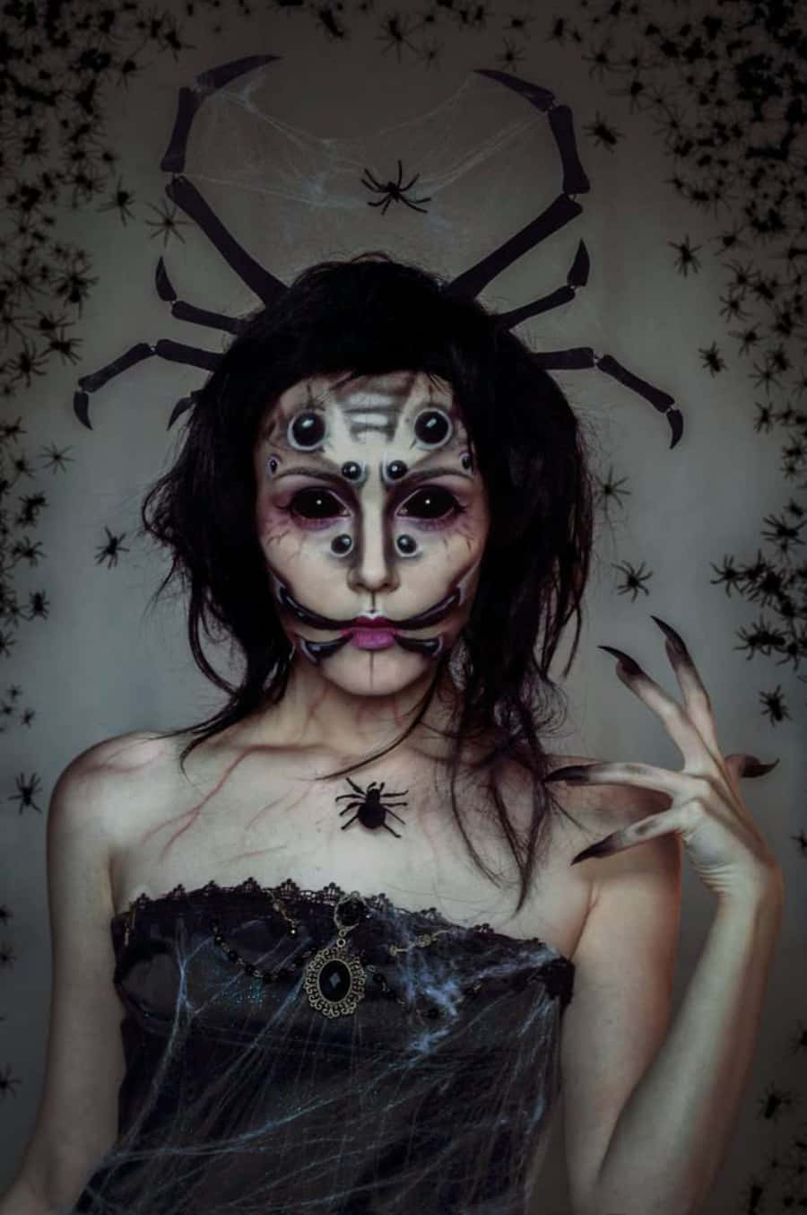 恐怖 桌布 壁紙 — 一位化著蜘蛛主題妝容、穿著蜘蛛服裝的女性，在一面佈滿蜘蛛和蜘蛛網的牆前擺姿勢。