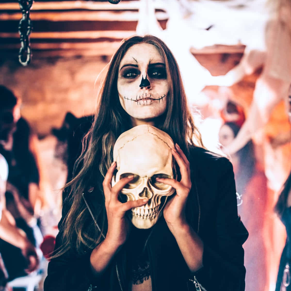 Creepy Halloween 桌布 壁紙 — 一位化著骷髏妝容的女性，在昏暗、煙霧瀰漫的萬聖節派對場景中手持一個人類頭骨。