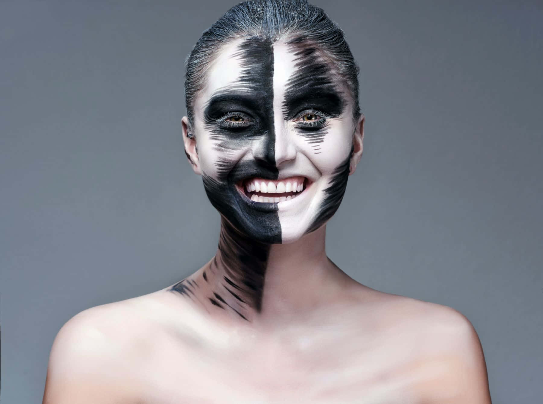 Halloween Face Paint 桌布 壁紙 — 一位半邊臉塗成黑白相間的女性在灰色背景前微笑。