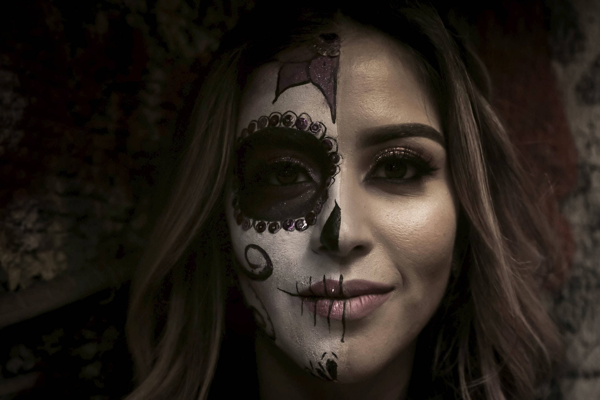 Mexican Woman 桌布 壁紙 — 一位半邊臉畫成糖骷髏的女人在深色花卉背景下溫柔微笑。