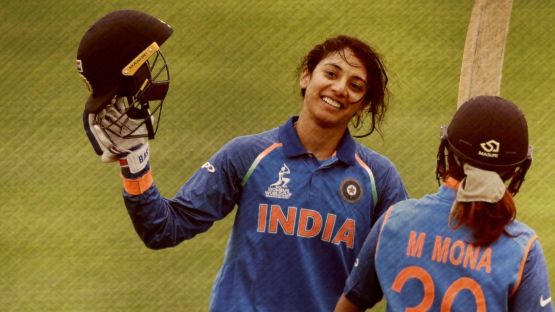 Smriti Mandhana 桌布 壁紙 — 一位印度女子板球運動員在綠色球場上高舉頭盔，滿臉喜悅。
