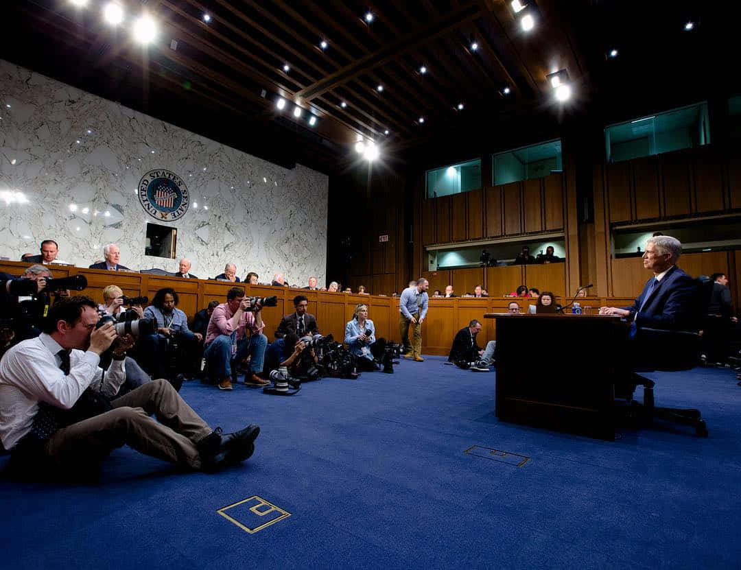 Speaker 桌布 壁紙 — 一位參議員在國會委員會面前作證，攝影師在正式的聽證室中捕捉這一刻。