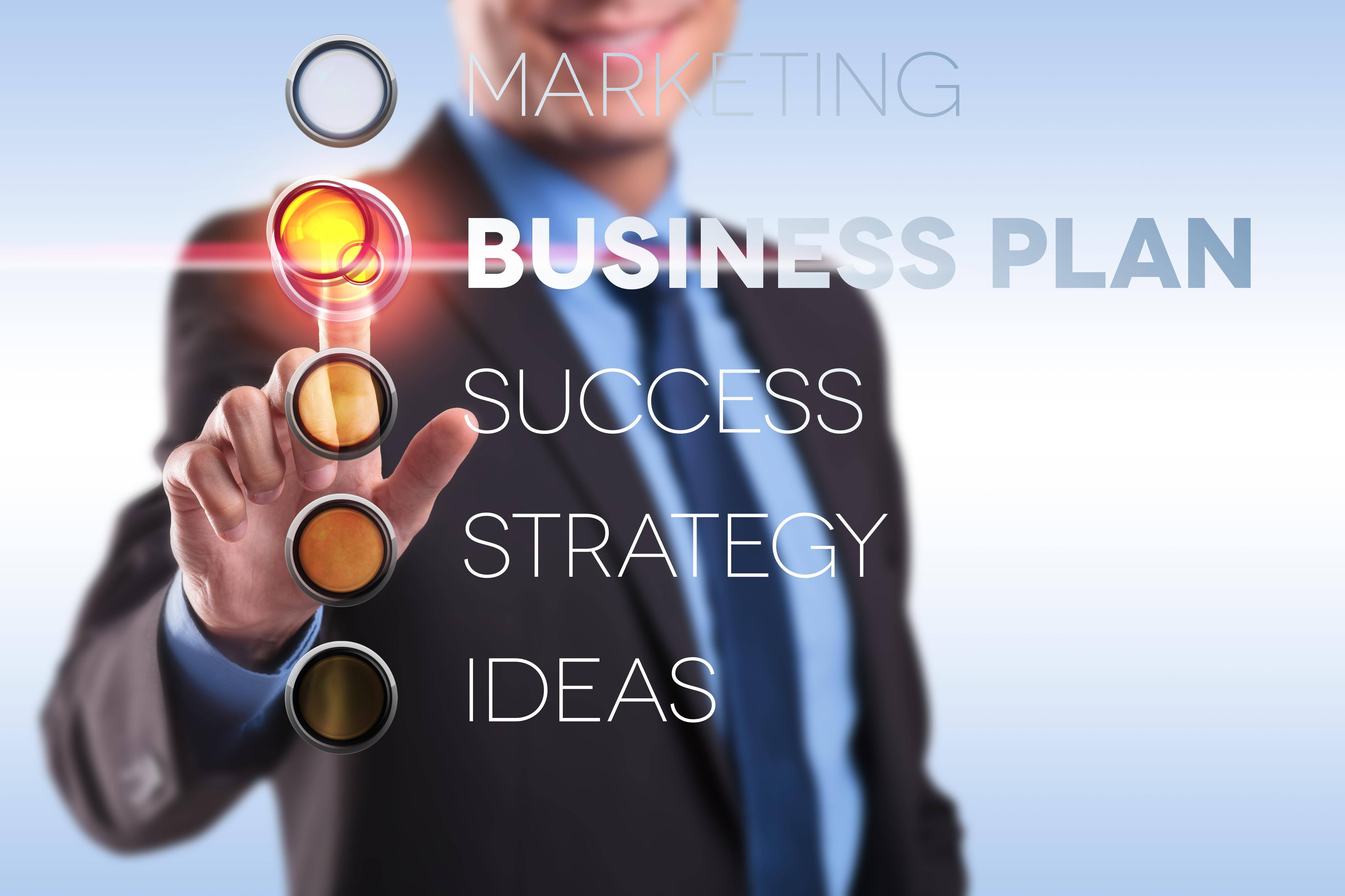 商業 桌布 壁紙 — 一位商人按下一個發光的按鈕，上面標有 'BUSINESS PLAN'，在一個帶有浮動文字關鍵詞的未來感介面上。