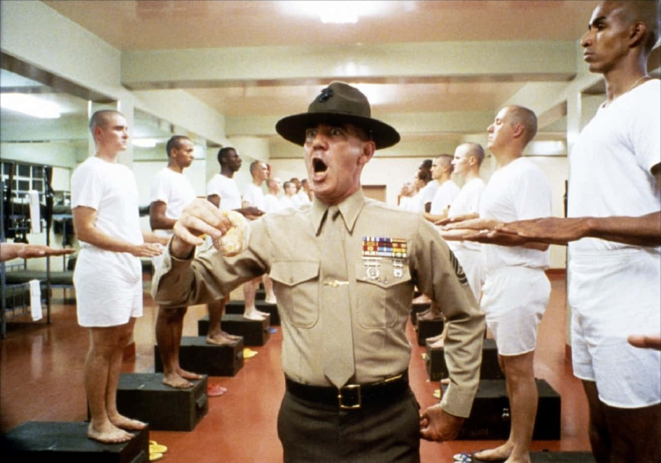 R. Lee Ermey 桌布 壁紙 — 一位嚴厲的訓練教官在室內新兵訓練期間對穿著白色制服的新兵大喊。