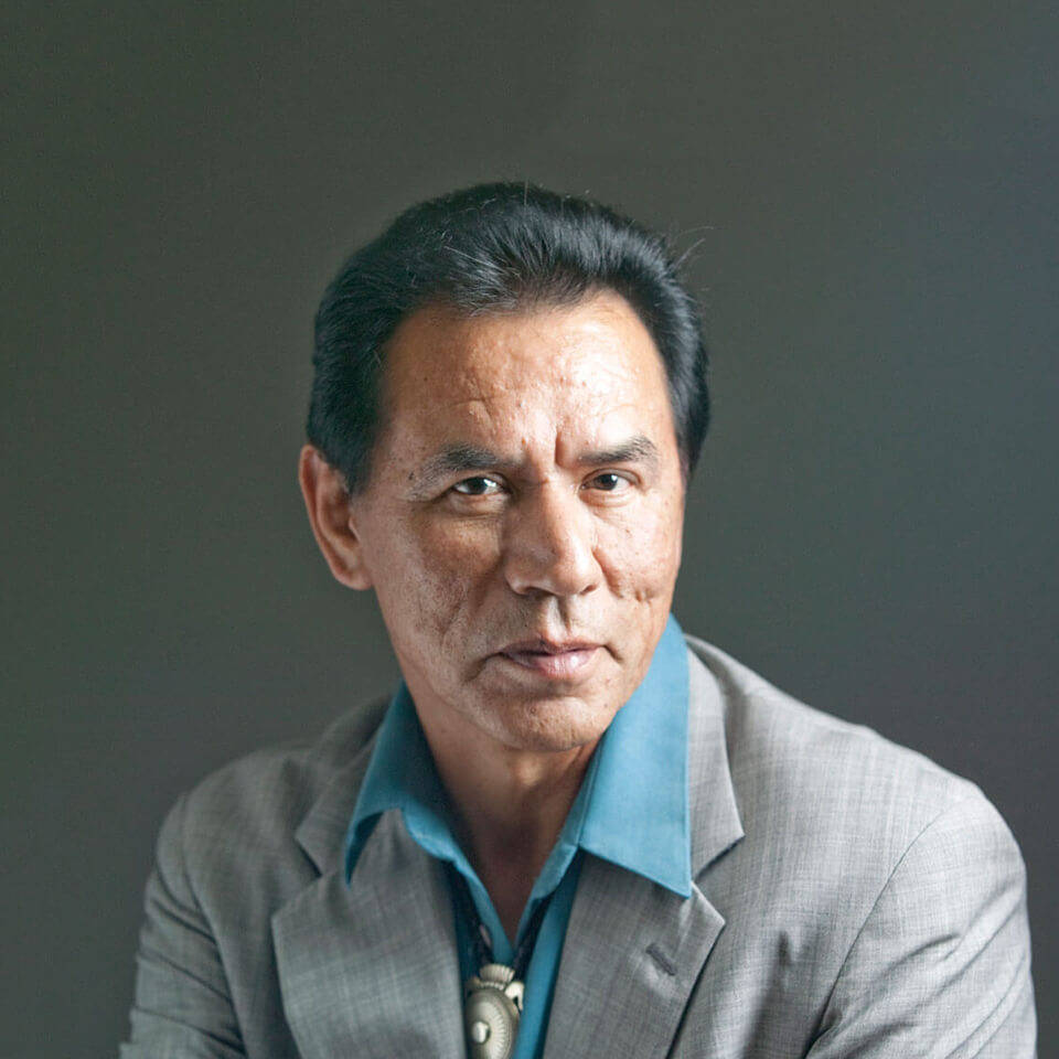 actor 桌布 壁紙 — 一位嚴肅的中年男子，深色頭髮，戴著銀色吊墜，在柔和的灰色背景下直視鏡頭。