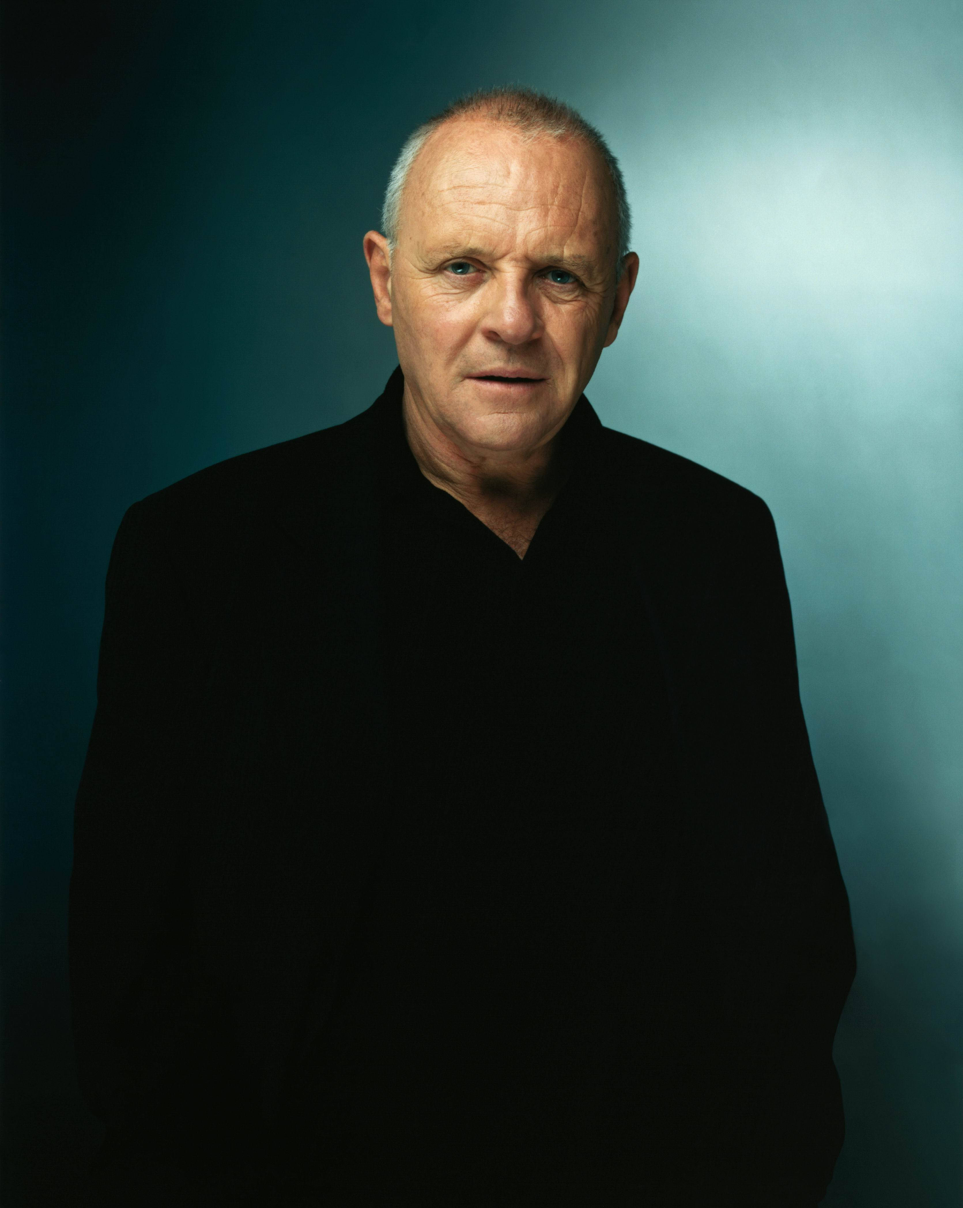 actor 桌布 壁紙 — 一位嚴肅的中年男子穿著黑色襯衫，站在漸層青綠色和藍色的攝影棚背景前，帶有戲劇性的燈光。