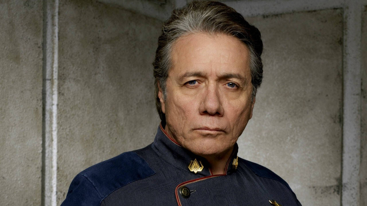 actor 桌布 壁紙 — 一位嚴肅的中年男子身穿深色制服，帶有金色徽章，在混凝土牆前直視鏡頭。
