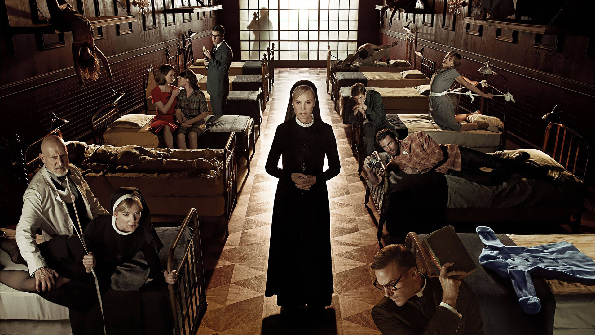 American Horror Story 桌布 壁紙 — 一位嚴肅的修女站在燈光昏暗的精神病房中央走廊，床上的病人在刺眼的天花板燈光下表現出令人不安的行為。
