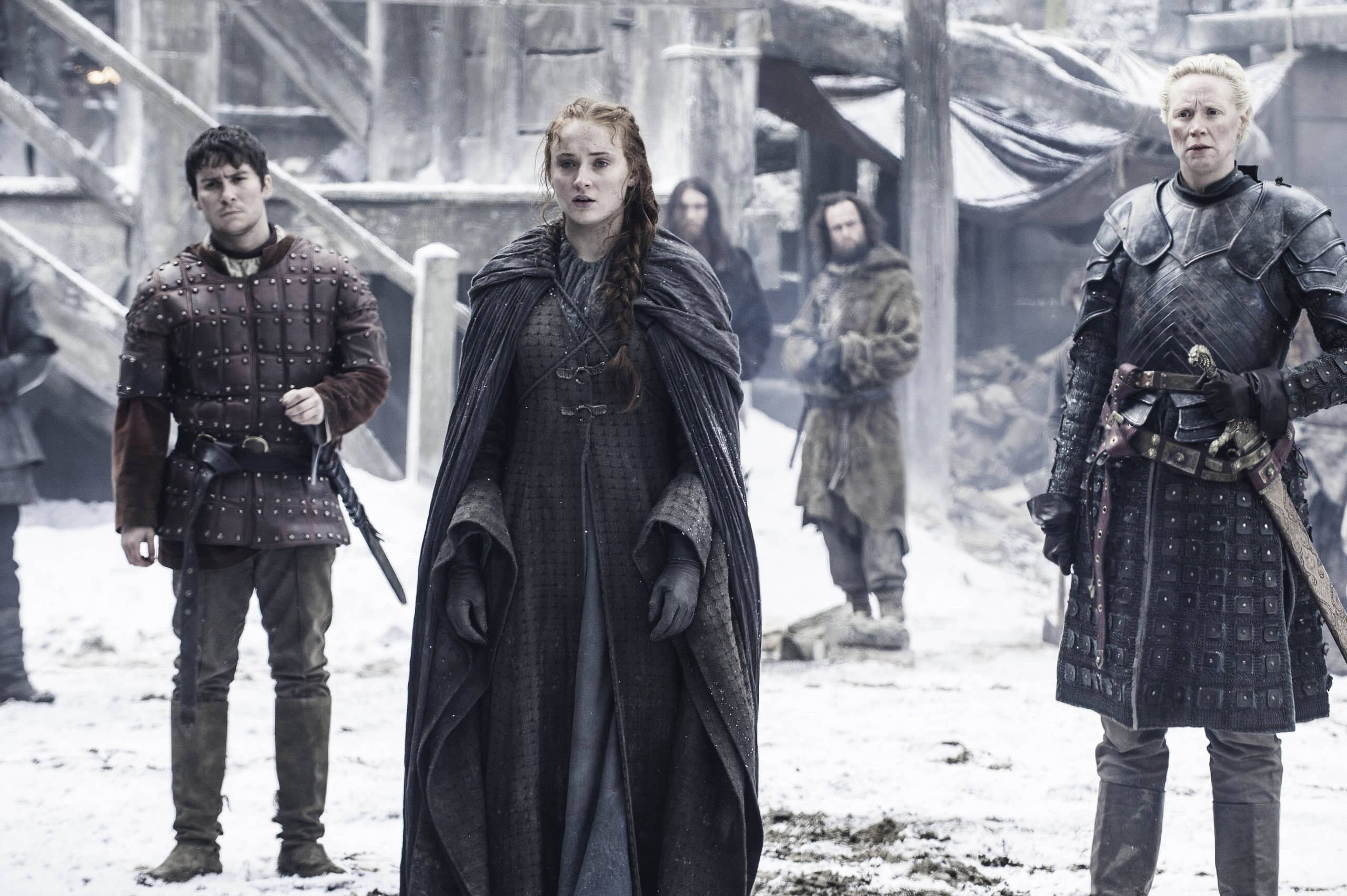 Sansa Stark 桌布 壁紙 — 一位嚴肅的女王身穿深色斗篷，與身穿盔甲的衛兵站在積雪的中世紀庭院中，天空多雲。