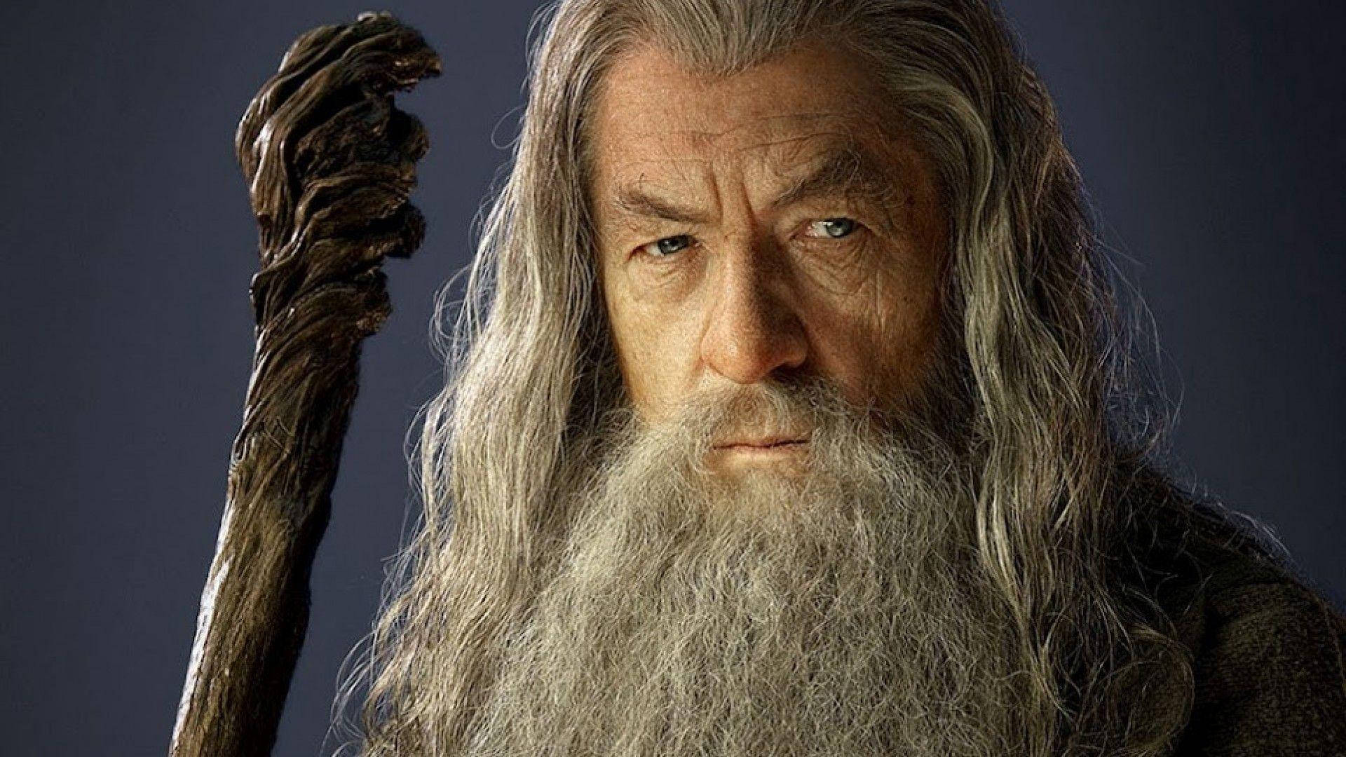 魔戒 桌布 壁紙 — 一位嚴肅的巫師，長著灰色長髮和鬍鬚，在深藍色背景下握著一根多節的法杖。