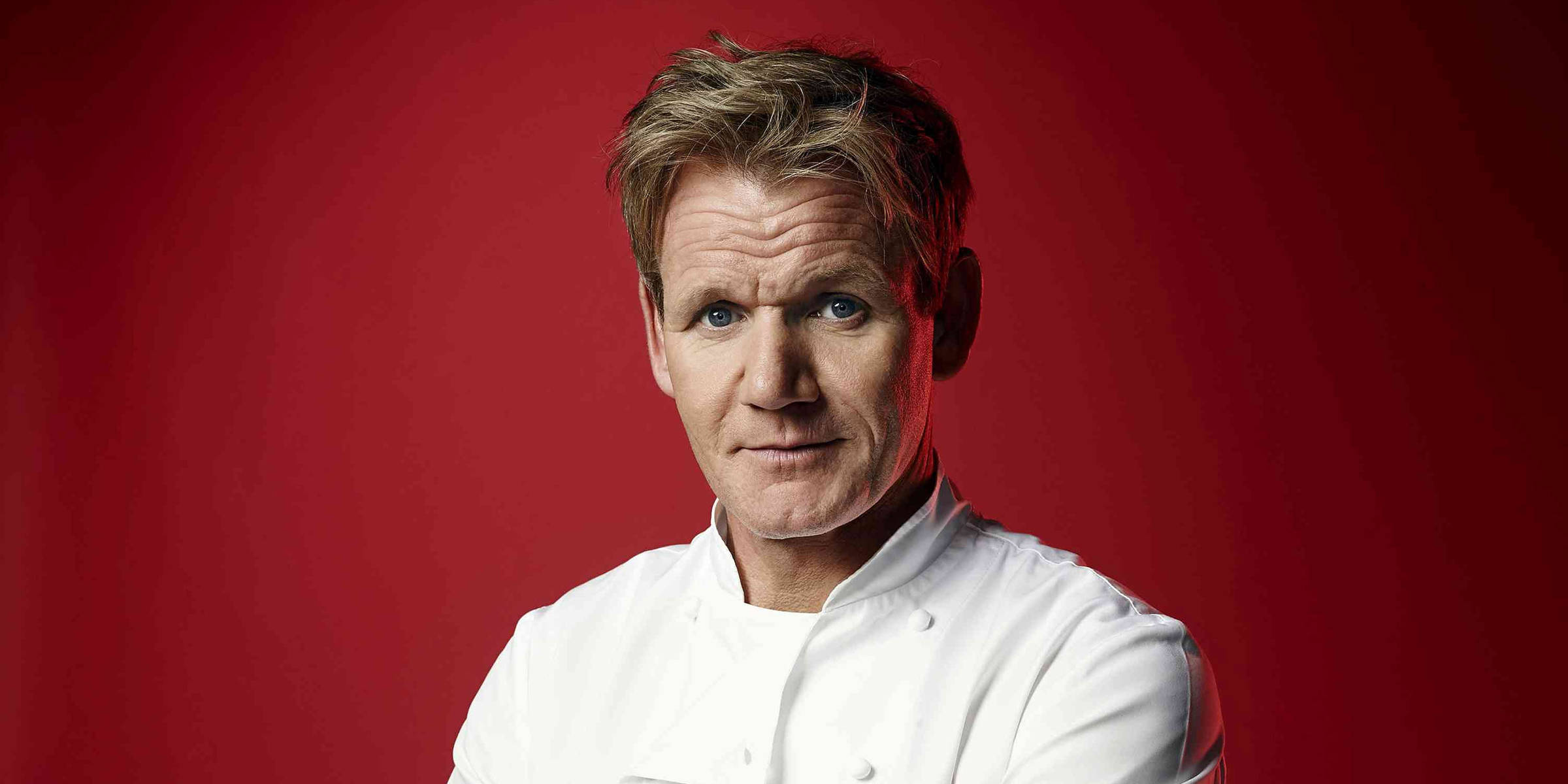 Gordon Ramsay 桌布 壁紙 — 一位嚴肅的廚師穿著白色外套，在鮮紅色的工作室背景下凝視著。