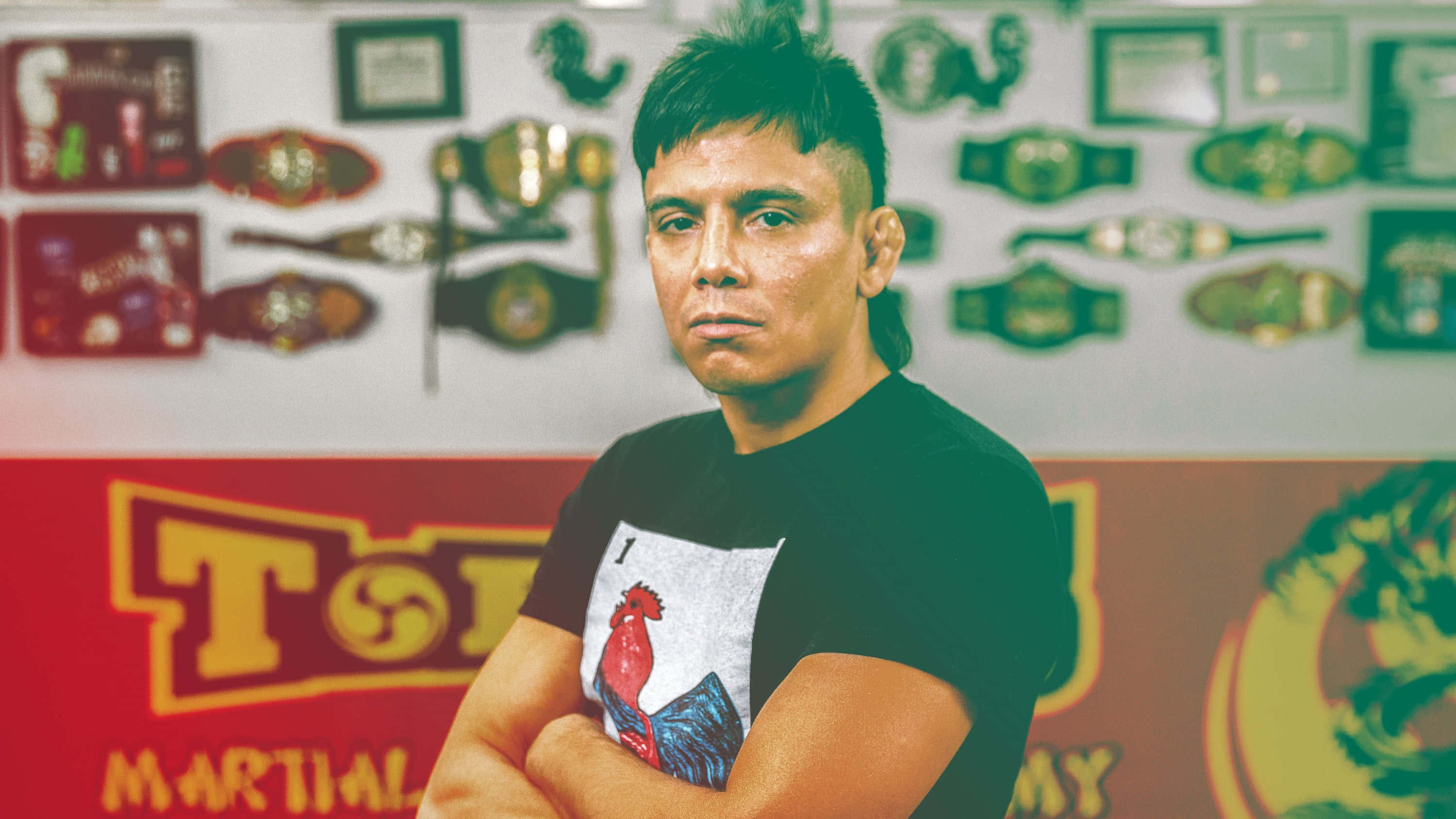 martial arts 桌布 壁紙 — 一位嚴肅的武術家交叉雙臂站在一面裝飾著冠軍腰帶和裱框獎項的牆前。