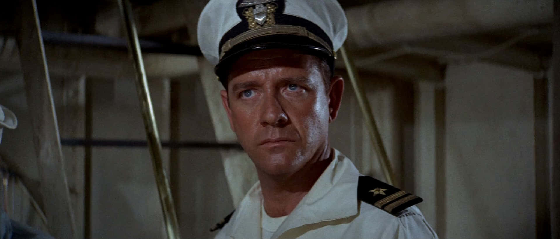 Richard Crenna 桌布 壁紙 — 一位嚴肅的海軍軍官身穿白色制服和帽子，在光線昏暗的船艙內凝視著。