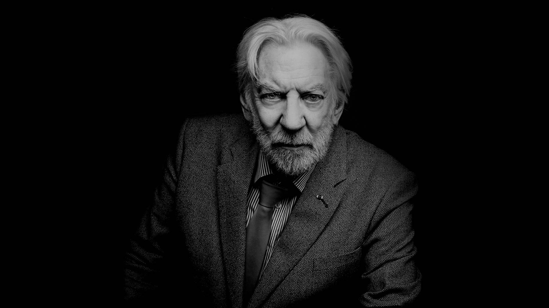 actor 桌布 壁紙 — 一位嚴肅的白髮白鬍子老人，在黑色背景下，以高對比度的黑白肖像照，目光銳利地凝視著。