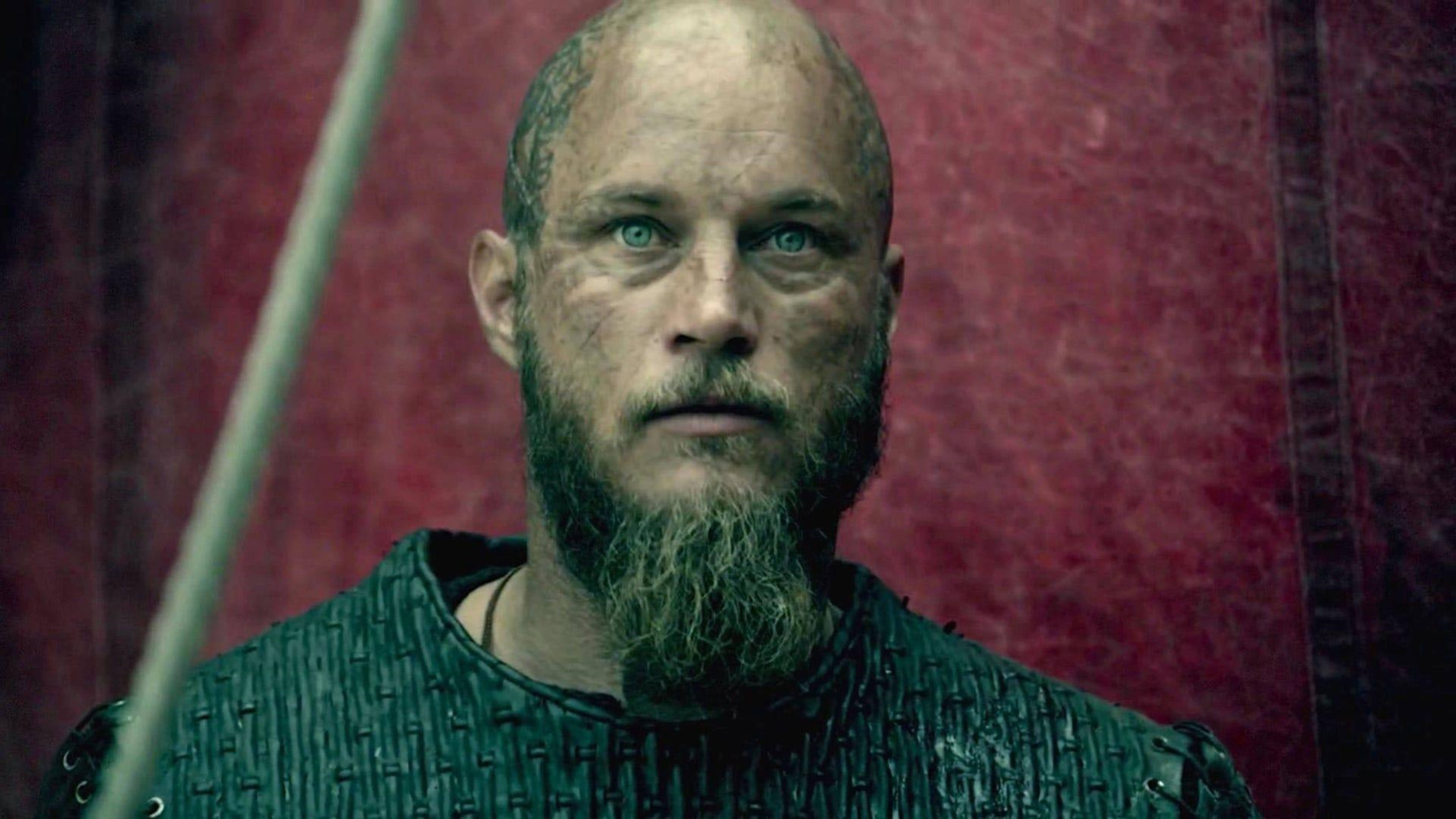 Vikings 桌布 壁紙 — 一位嚴肅的維京戰士，留著長鬍鬚和綠色眼睛，在深紅色紋理背景前強烈凝視。