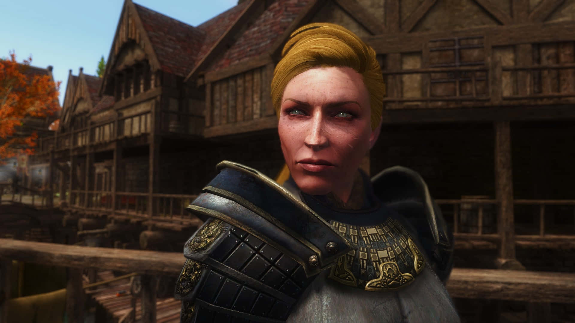 Skyrim Delphine 桌布 壁紙 — 一位嚴肅的金髮盔甲女子站在一個有木造建築和秋葉的質樸中世紀小鎮中。
