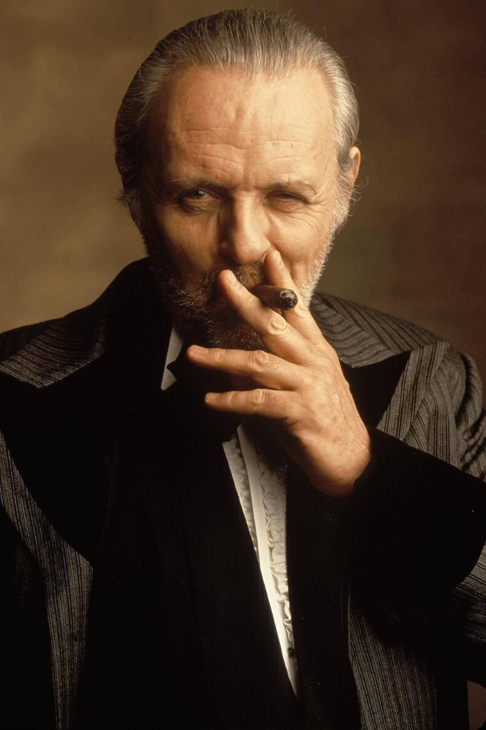 actor 桌布 壁紙 — 一位嚴肅的長者，灰白頭髮和鬍鬚，穿著深色細條紋西裝，在溫暖的棕色背景下抽雪茄。