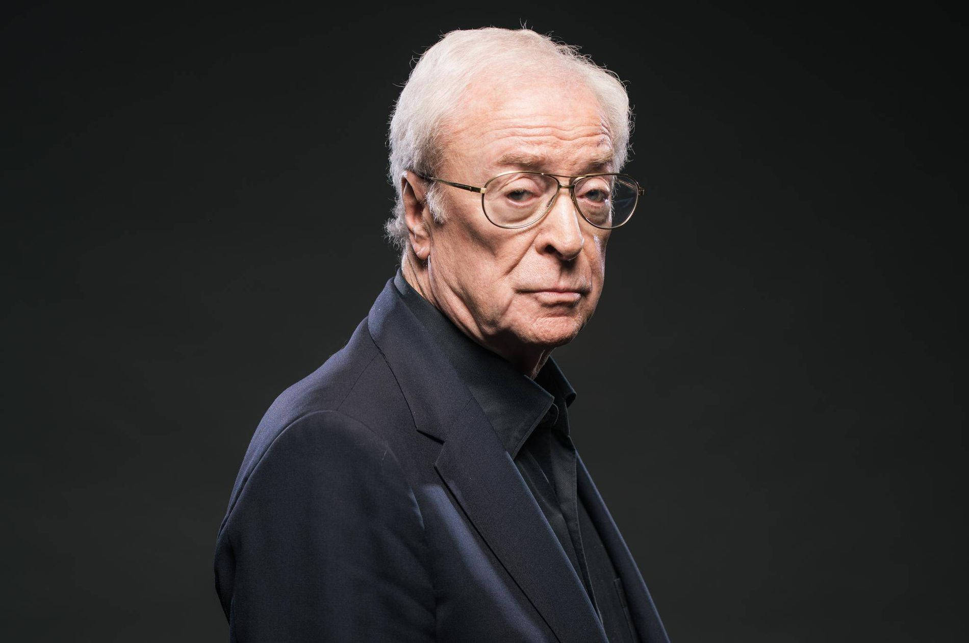 actor 桌布 壁紙 — 一位嚴肅的長者，白髮戴眼鏡，在深色背景下凝視著。