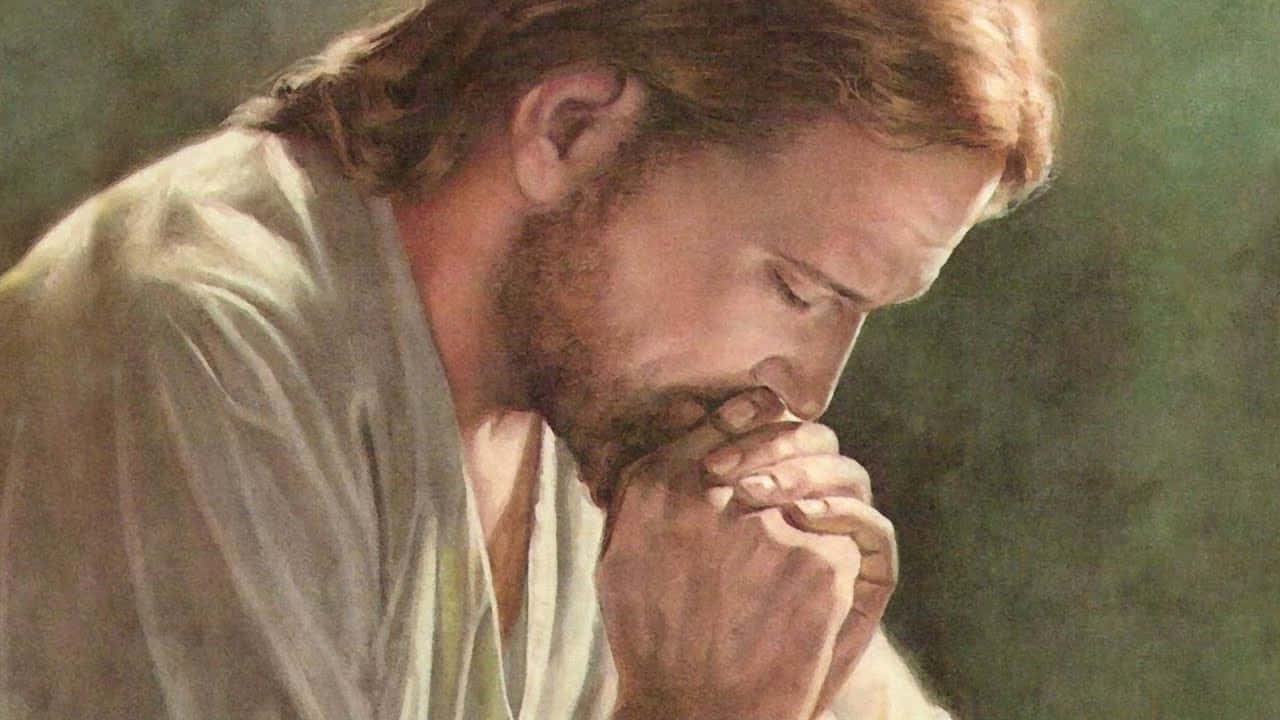 Jesus Praying 桌布 壁紙 — 一位嚴肅的長髮鬍鬚男子跪著祈禱，雙手合十靠近嘴邊，處於柔和光線、低調綠色的環境中。