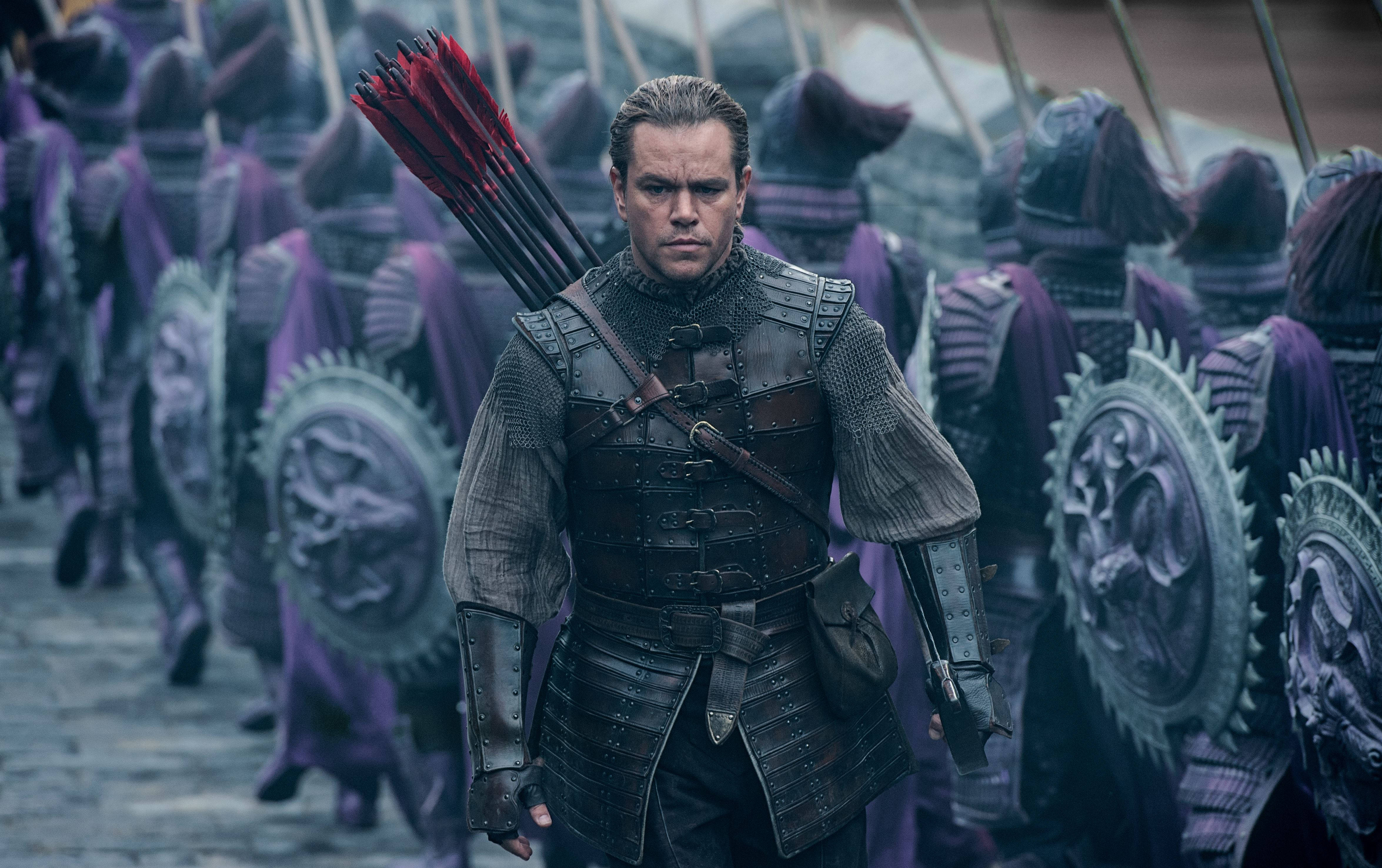 Matt Damon 桌布 壁紙 — 一位嚴肅的騎士身穿黑色盔甲，站在一排身穿紫色衣服、手持盾牌和長矛的士兵面前。